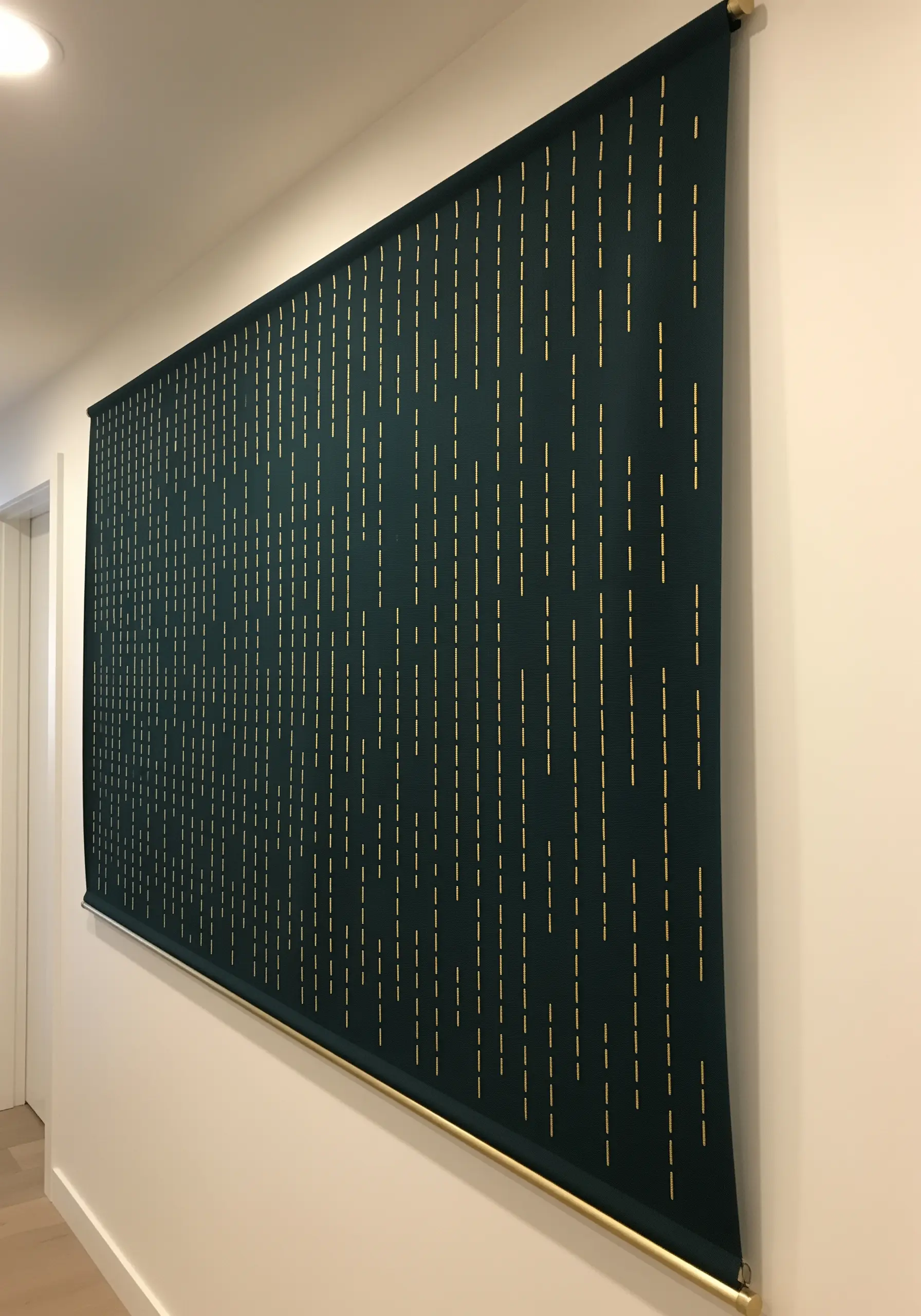 A large dark green wall hanging with a pattern of vertical gold running stitches.