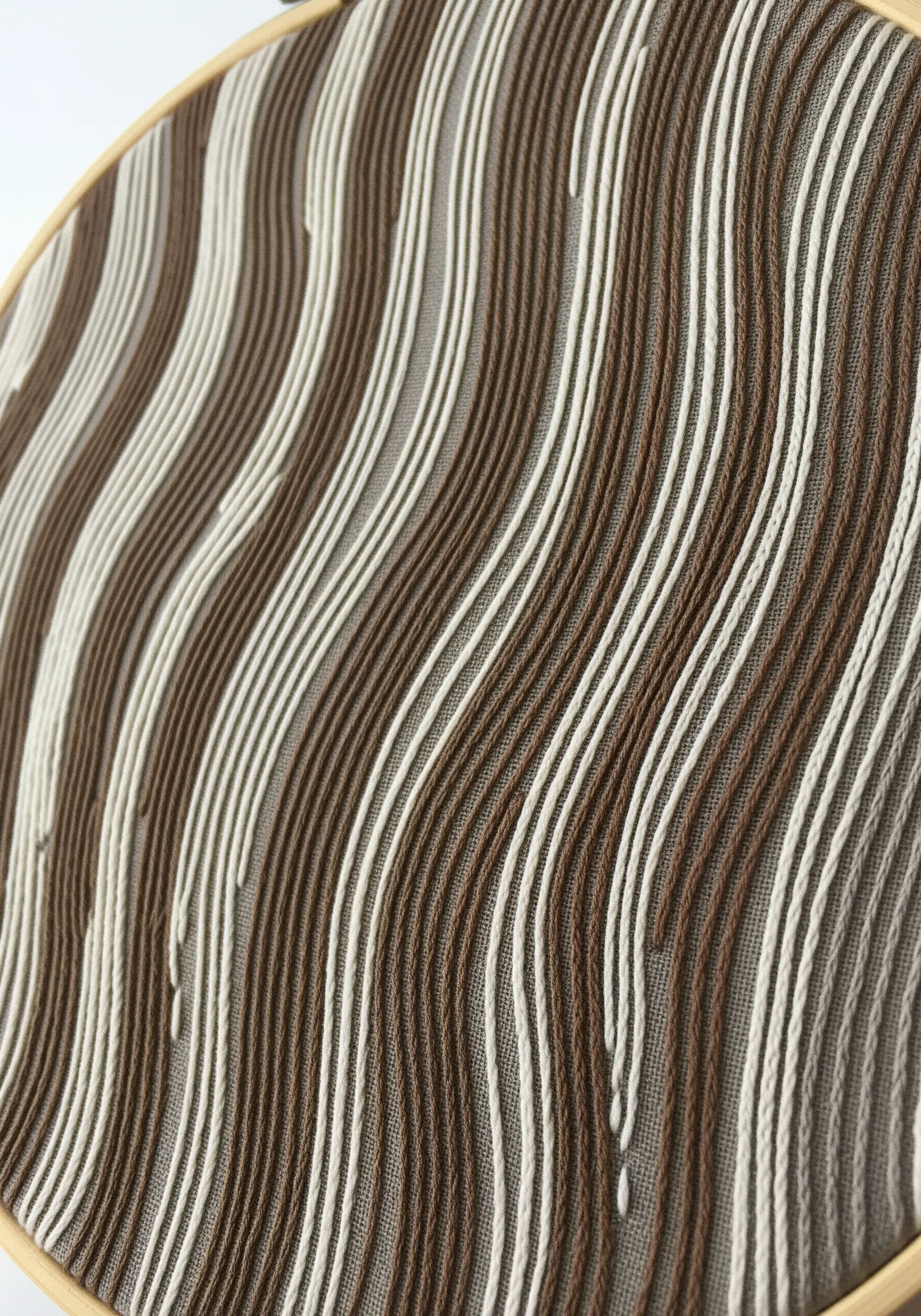 Abstract embroidery of wavy vertical lines in brown and white on a neutral fabric.