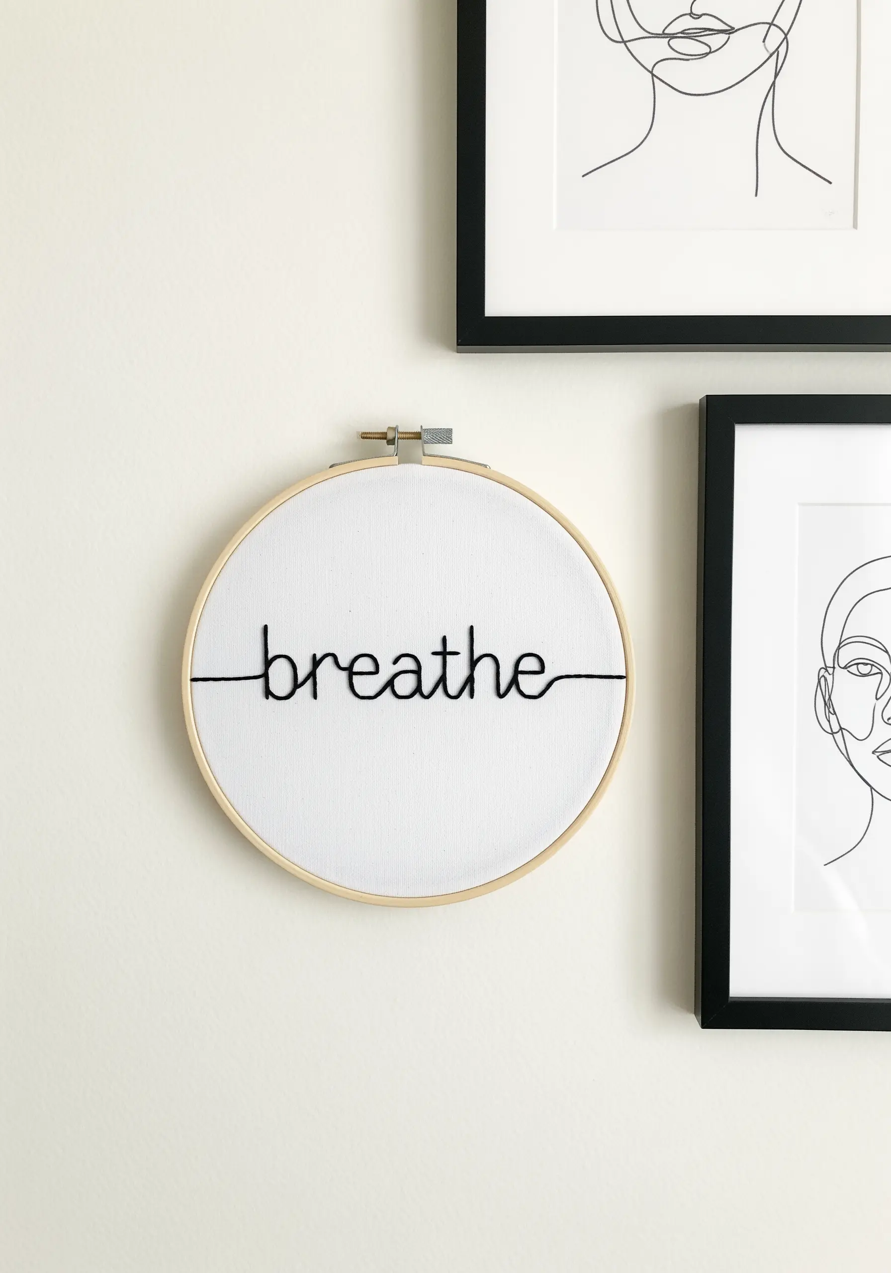The word 'breathe' stitched in bold black thread across a white fabric hoop.