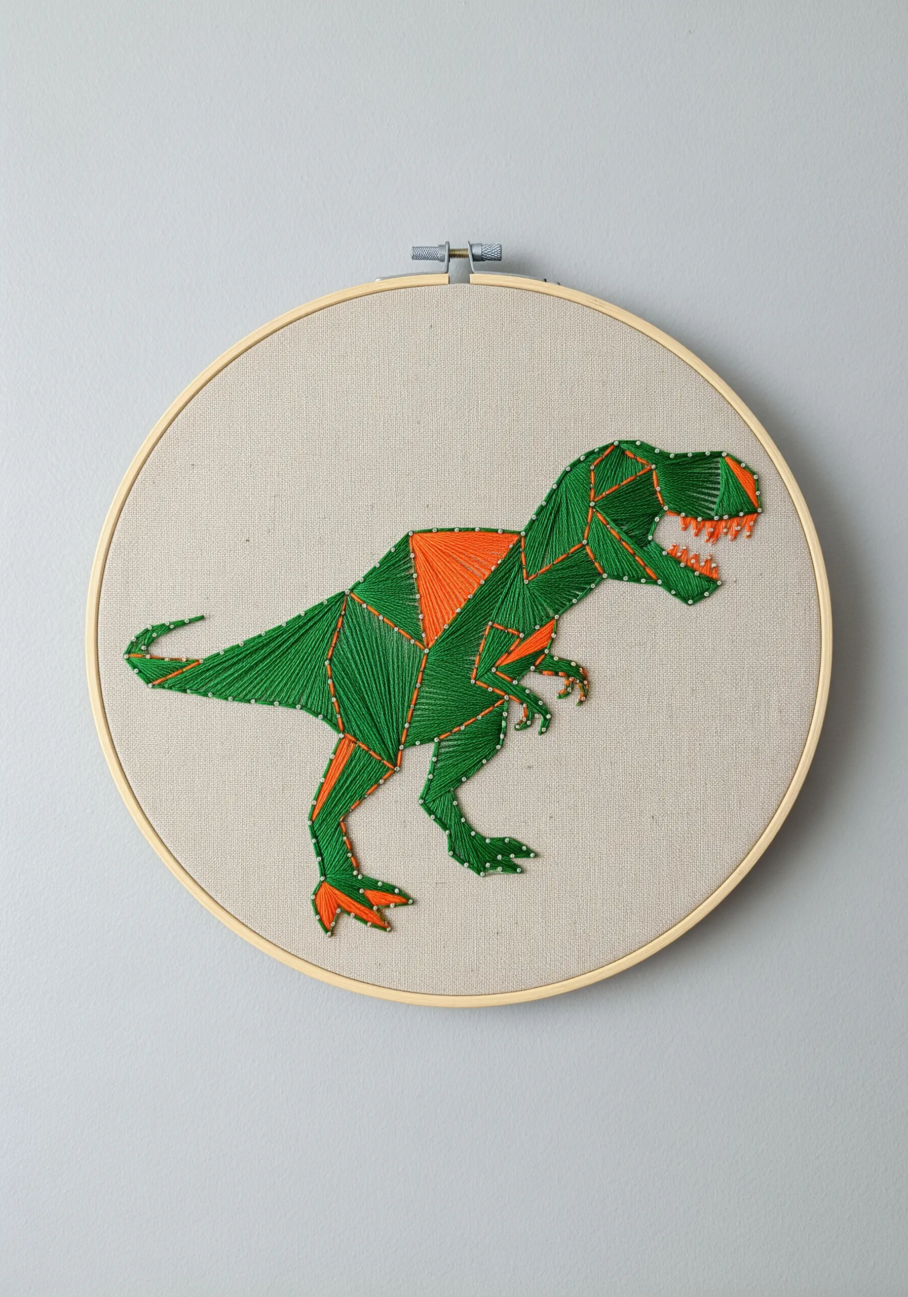 A geometric T-Rex embroidered with crisp, faceted sections of green and orange satin stitch.