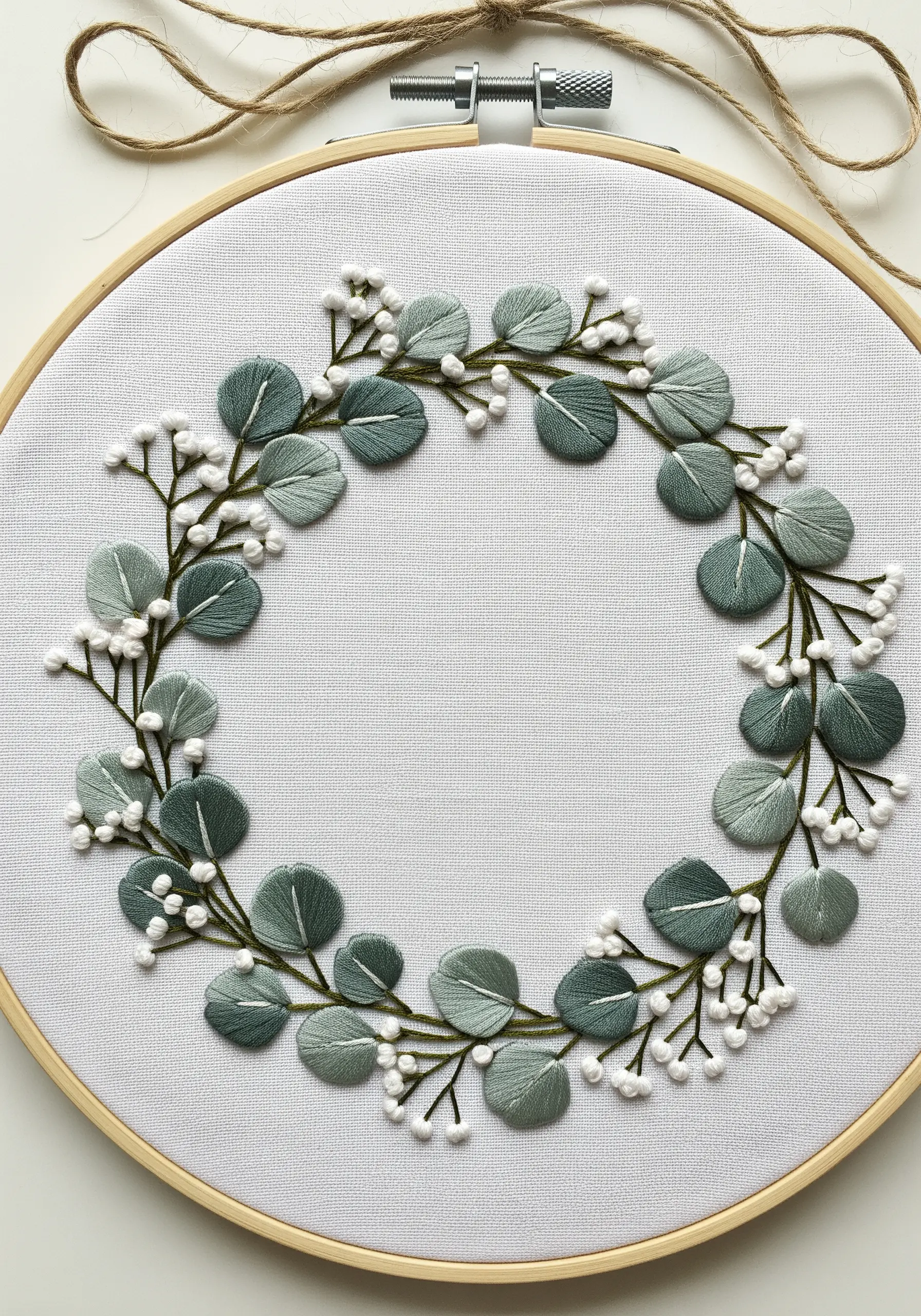 A delicate wreath of embroidered eucalyptus leaves and white baby's breath flowers.