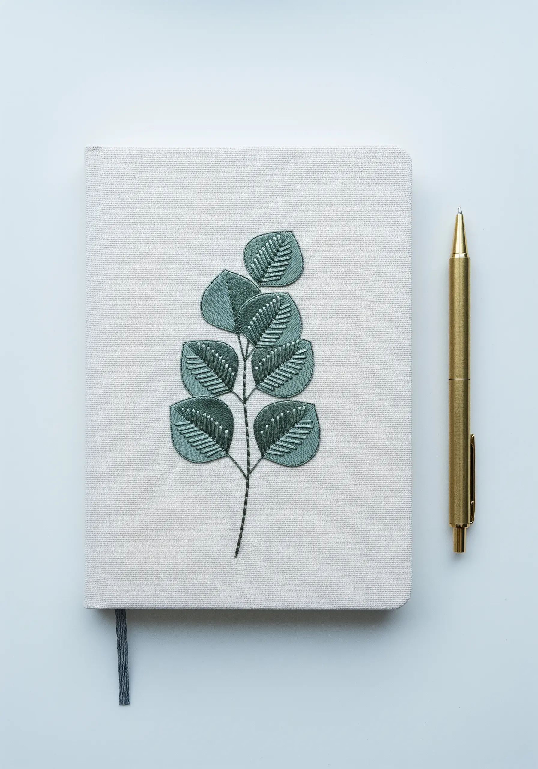 A tone-on-tone embroidery of eucalyptus leaves on a fabric-covered notebook.