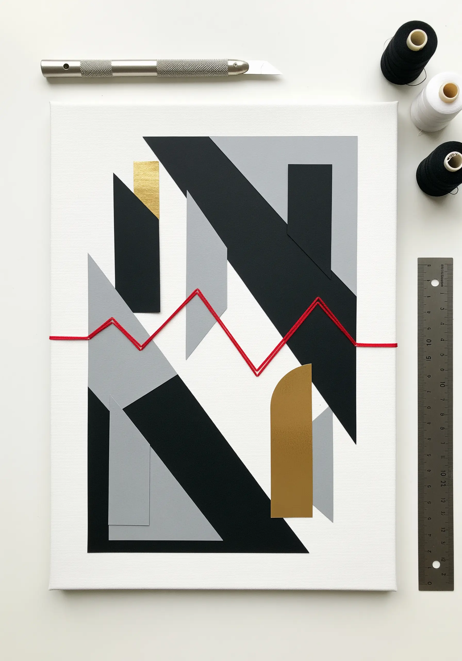 An abstract collage of black, grey, and gold paper with a single red thread stretched across it.
