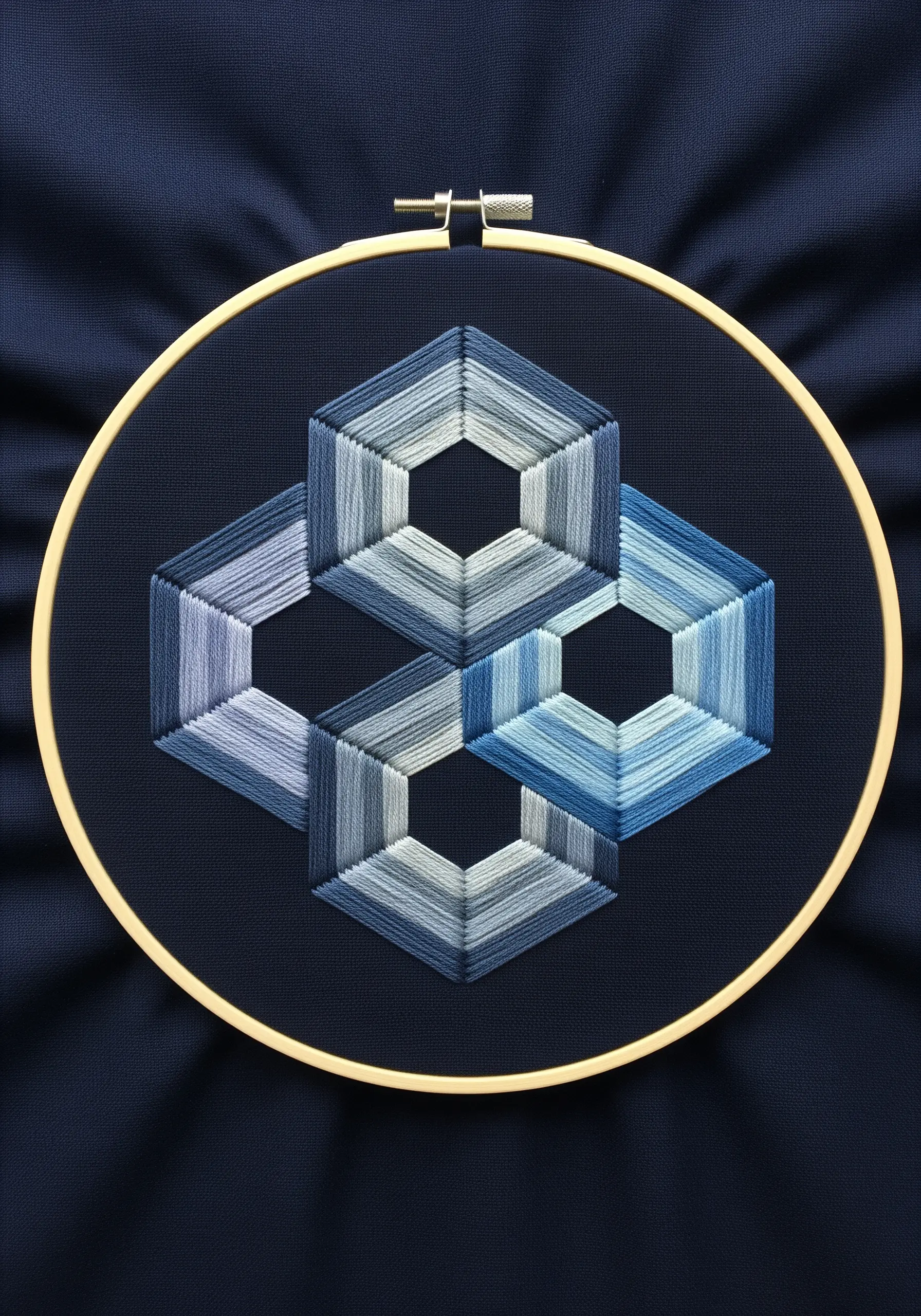 Geometric embroidery of overlapping hexagons in blue and grey gradients on navy fabric.