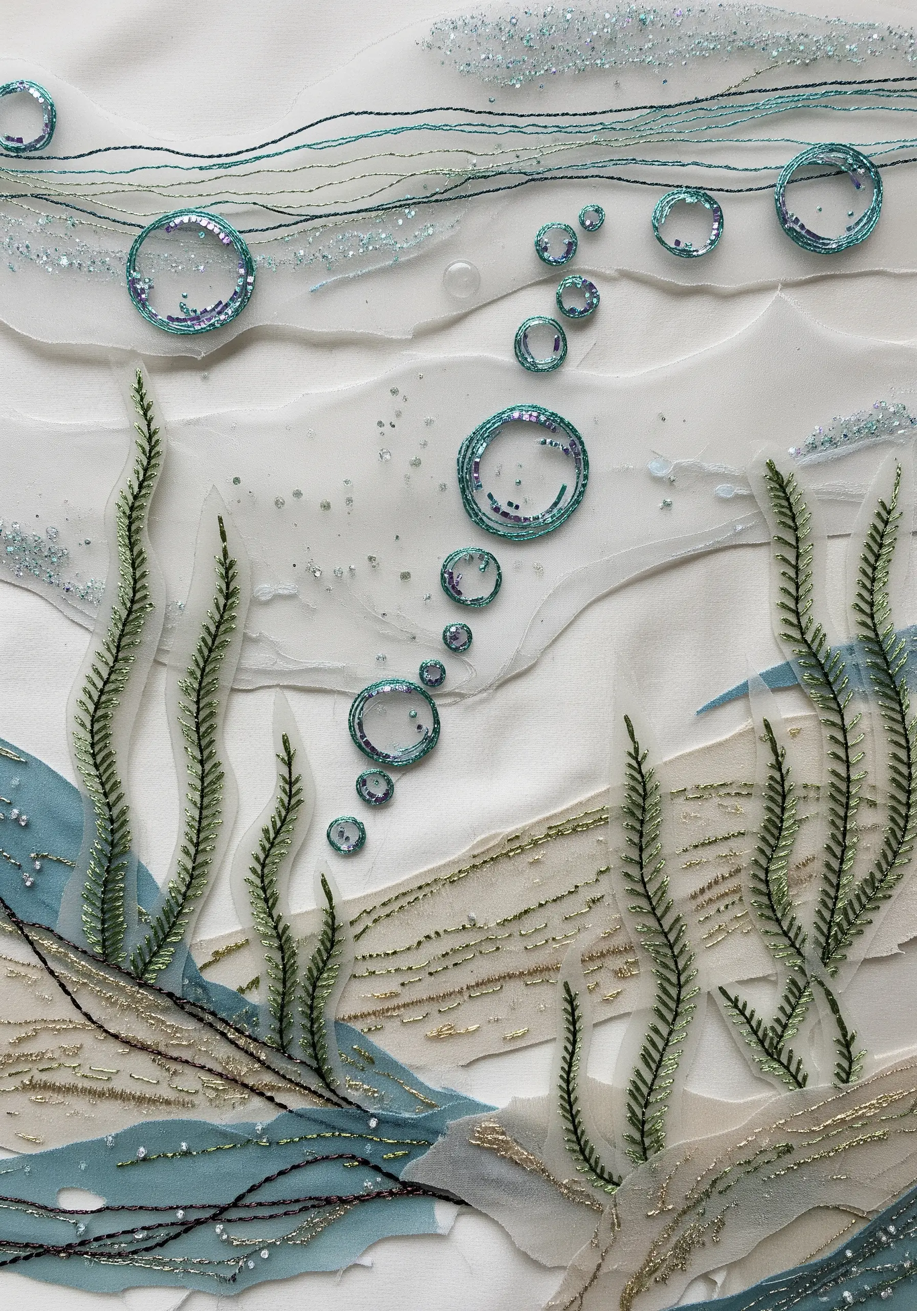 A mixed-media embroidery of an underwater scene with sheer fabrics, metallic threads, and sequins.
