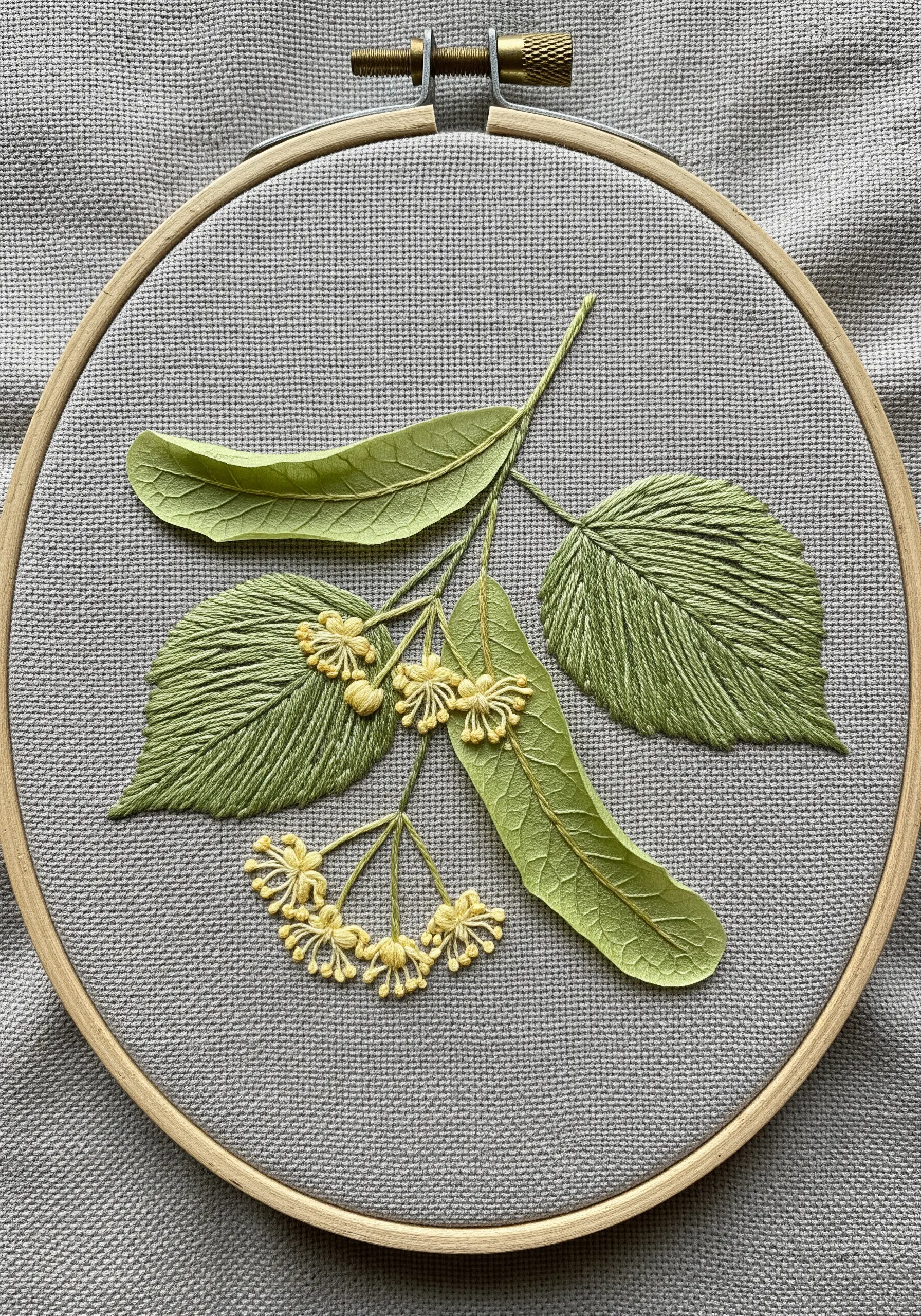 A 3D stumpwork embroidery of a linden branch with detached, wired leaves.