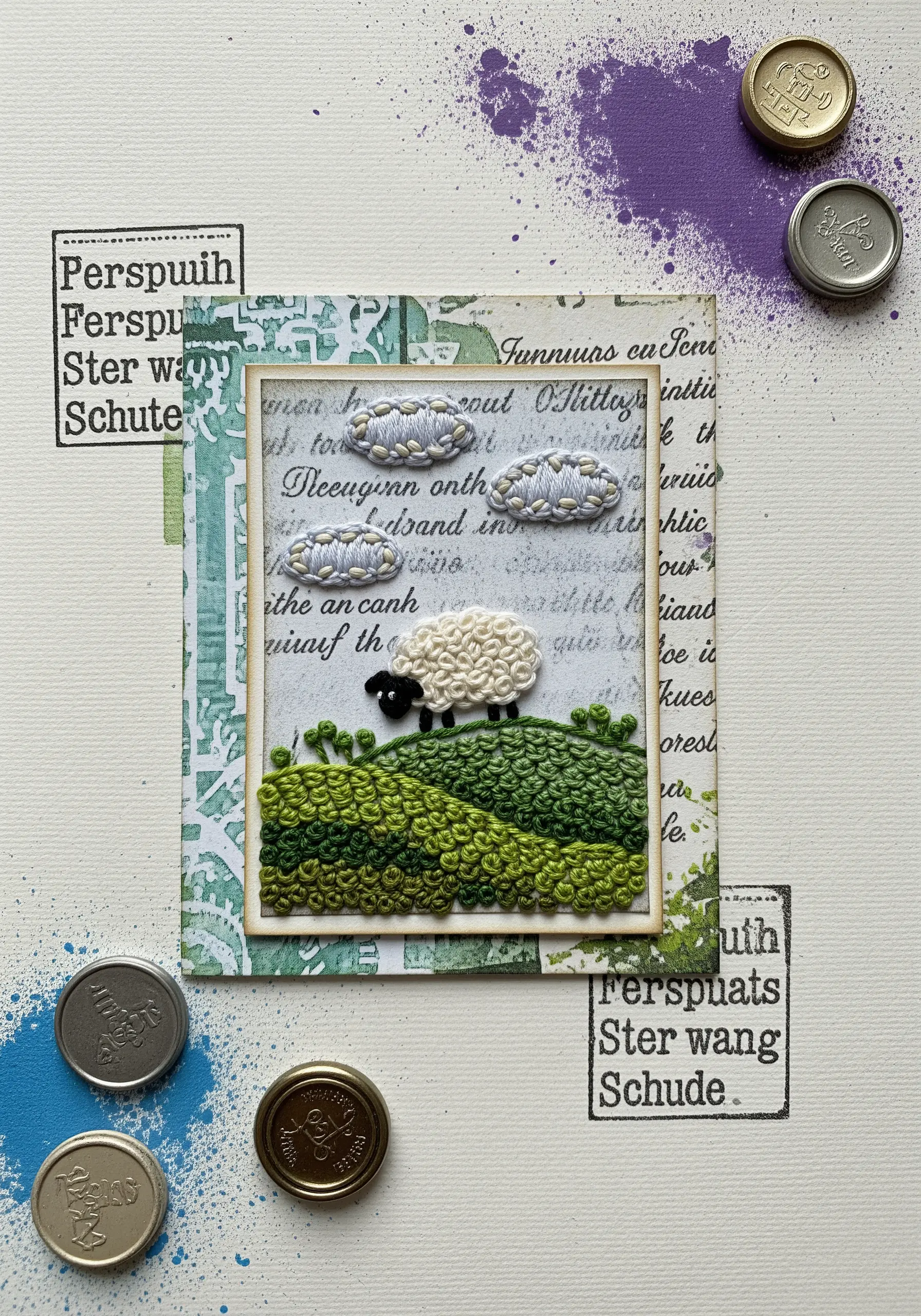 An embroidered sheep on a hill, framed and mounted on a mixed-media art card.