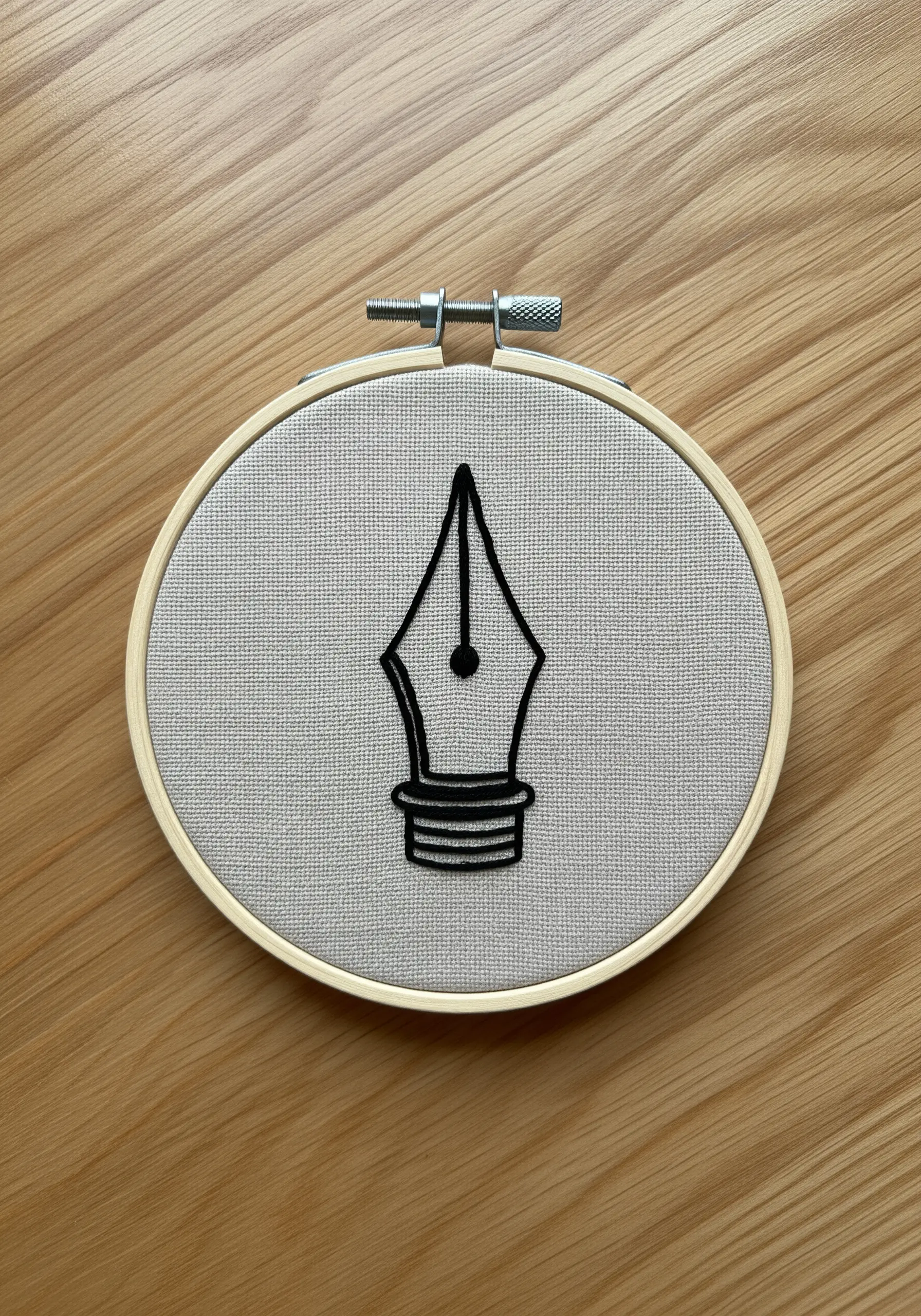 A black fountain pen nib embroidered with a bold, clean satin stitch outline.
