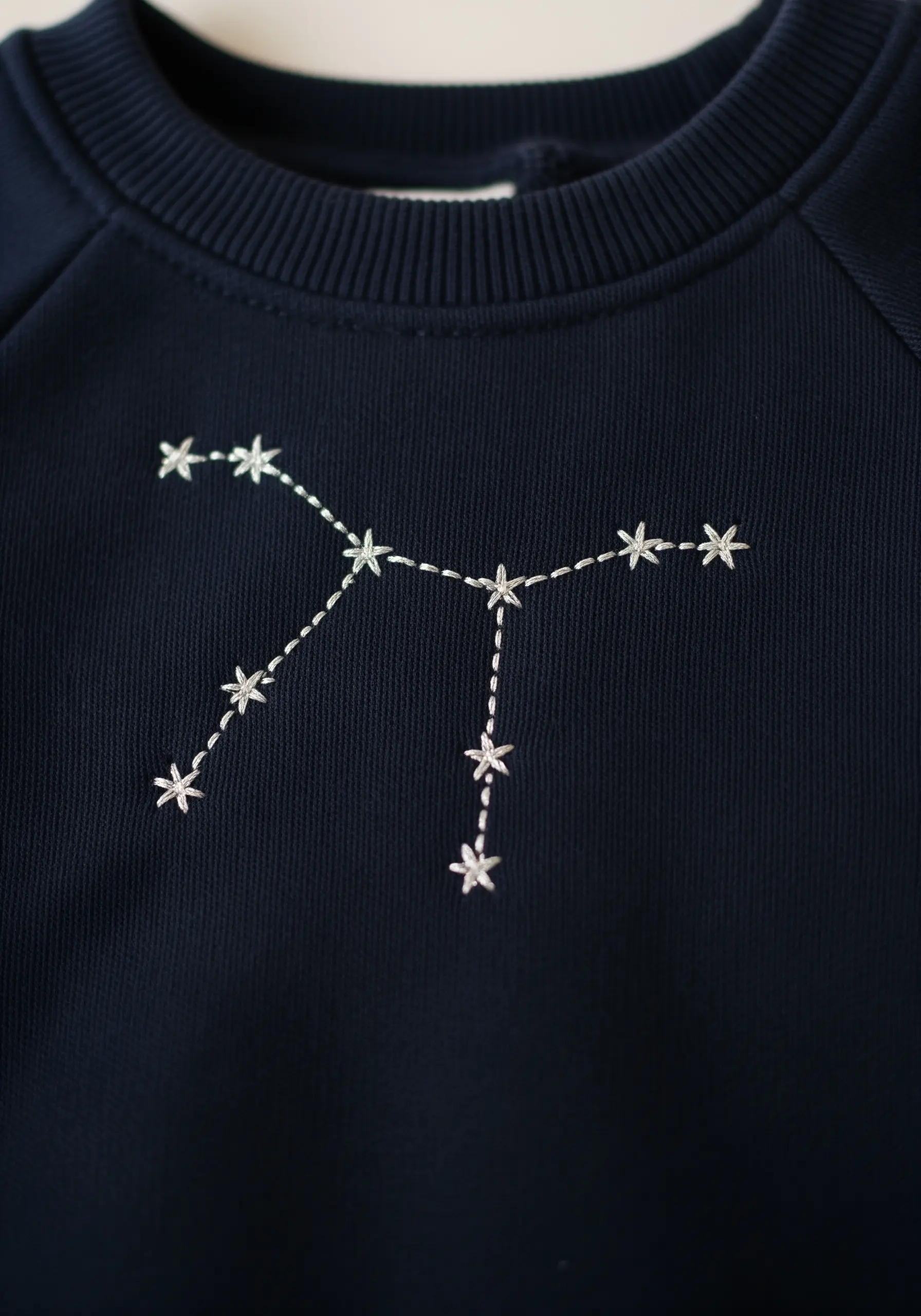 Silver thread constellation embroidered on a dark navy blue sweatshirt.