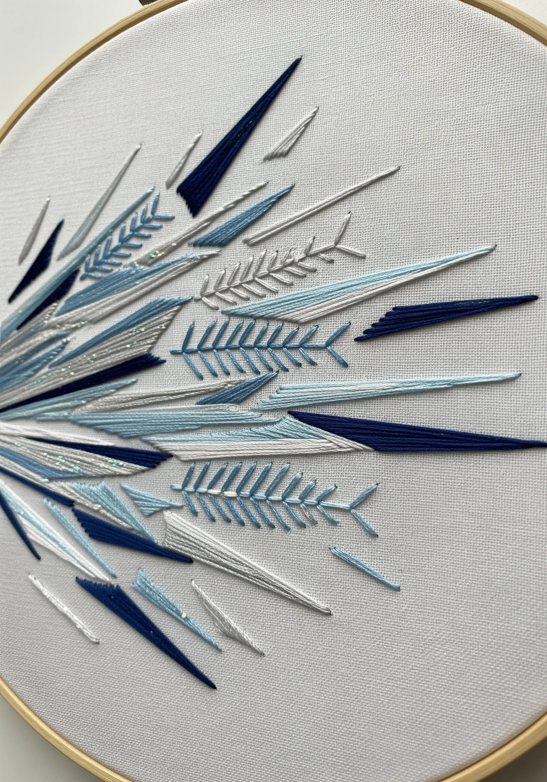 Abstract explosion of blue, white, and silver satin stitch shards and fern stitches.