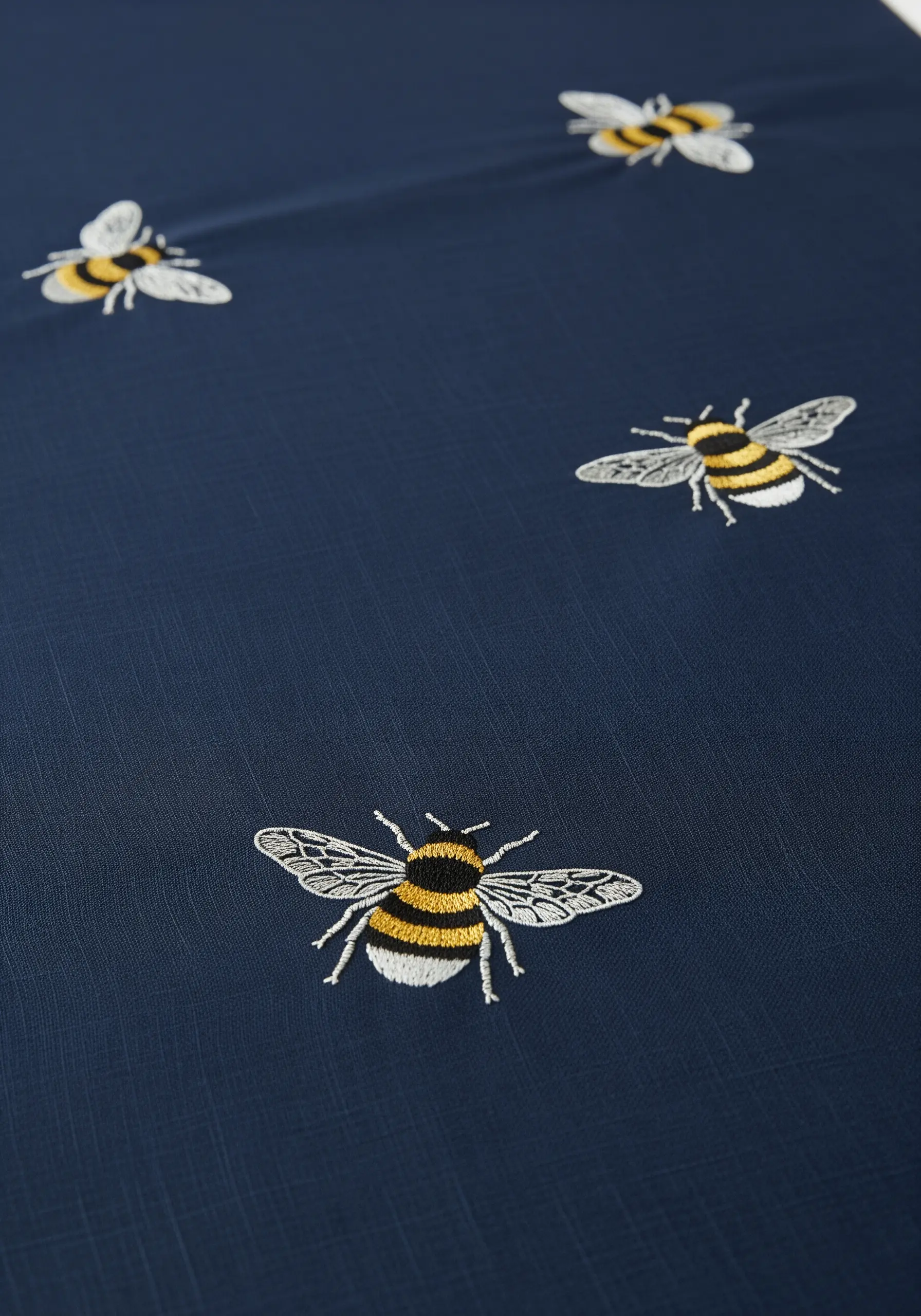 Embroidered bees with translucent-looking wings scattered across a dark blue tablecloth.