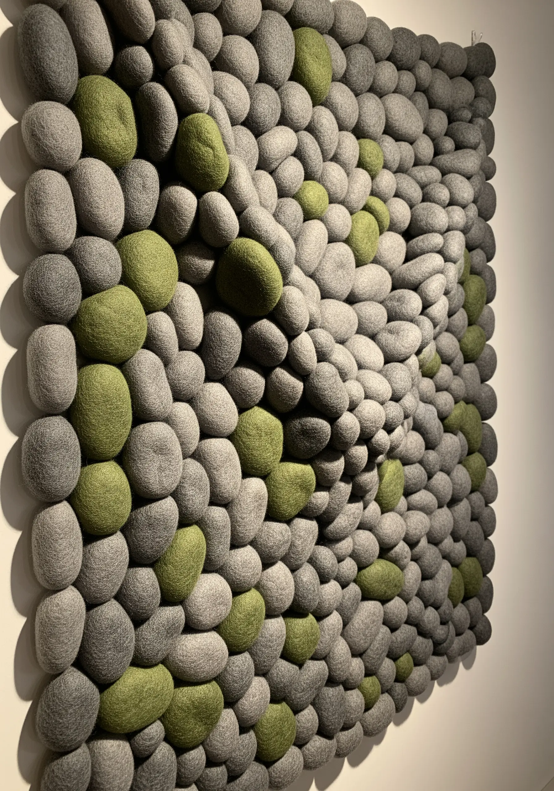 A wall panel covered in tightly packed grey and green felted wool 'pebbles'.