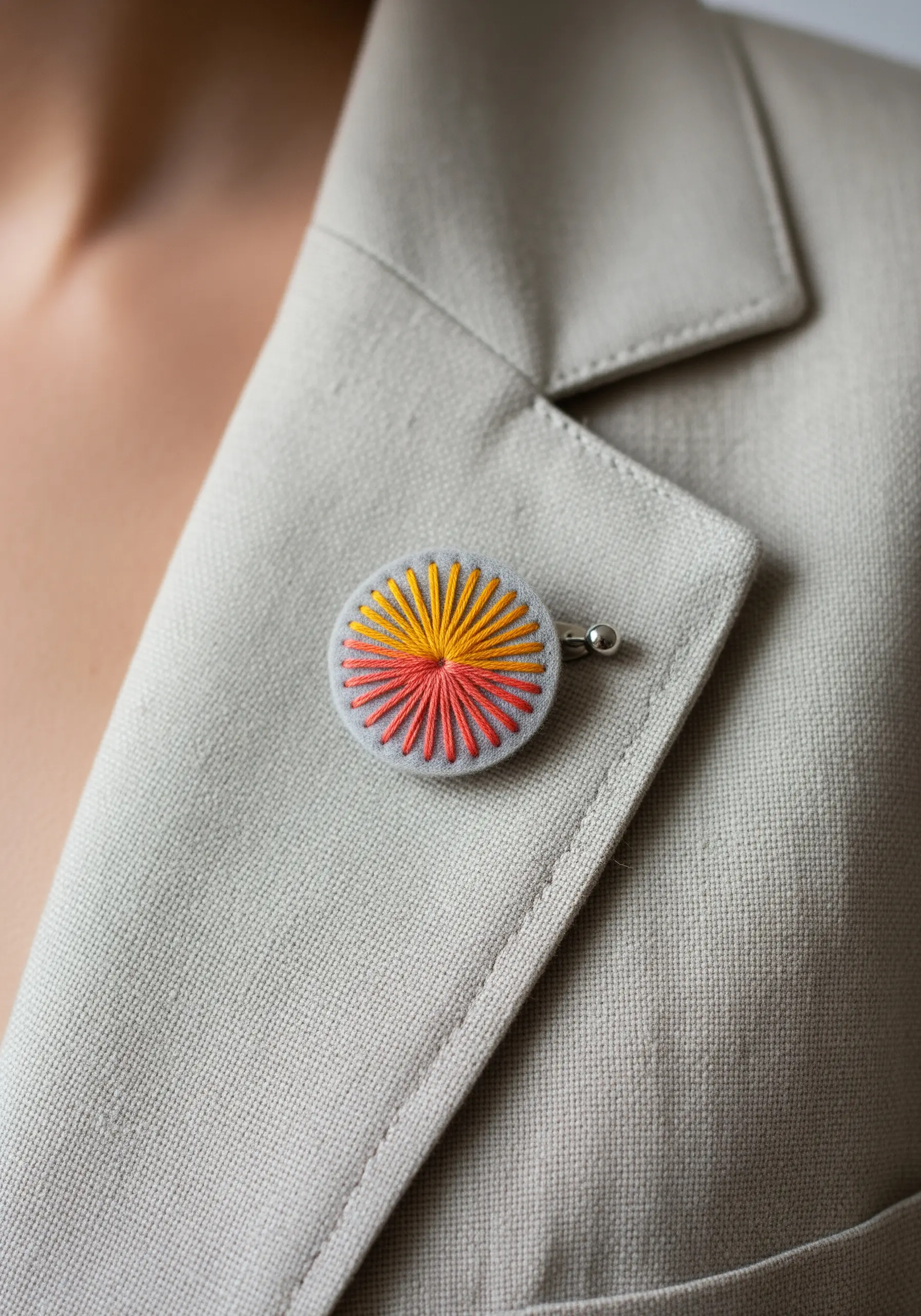 A small, round embroidered pin with a radiating sunburst pattern in yellow, orange, and red.