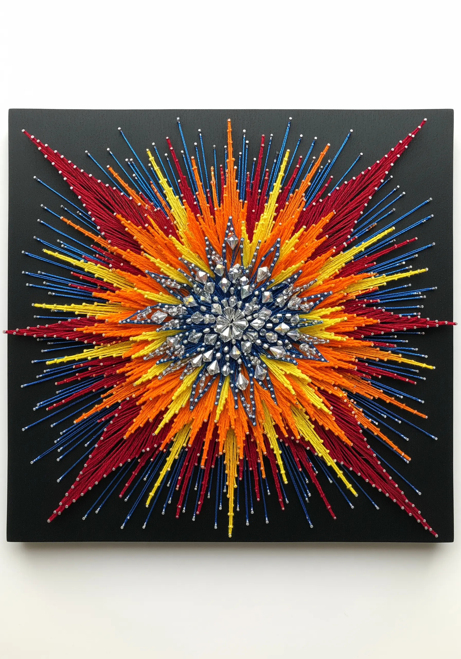 A starburst string art piece with a crystal center and red, orange, yellow, and blue threads.