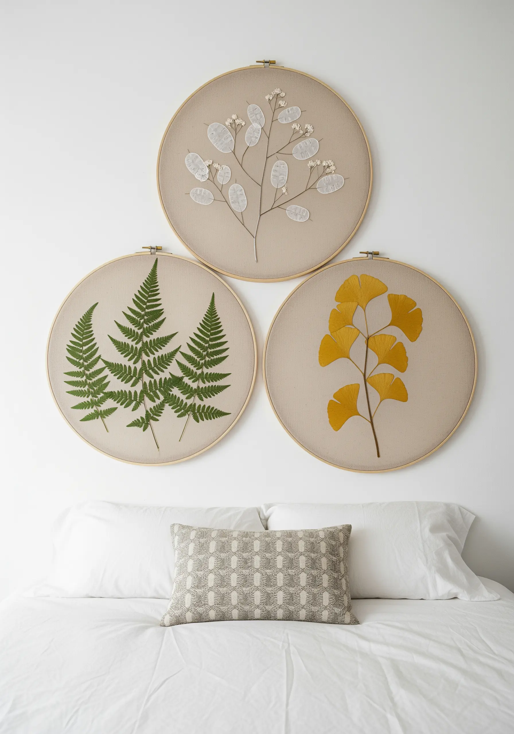 A triptych of embroidery hoops displaying real pressed fern, lunaria, and ginkgo leaves.