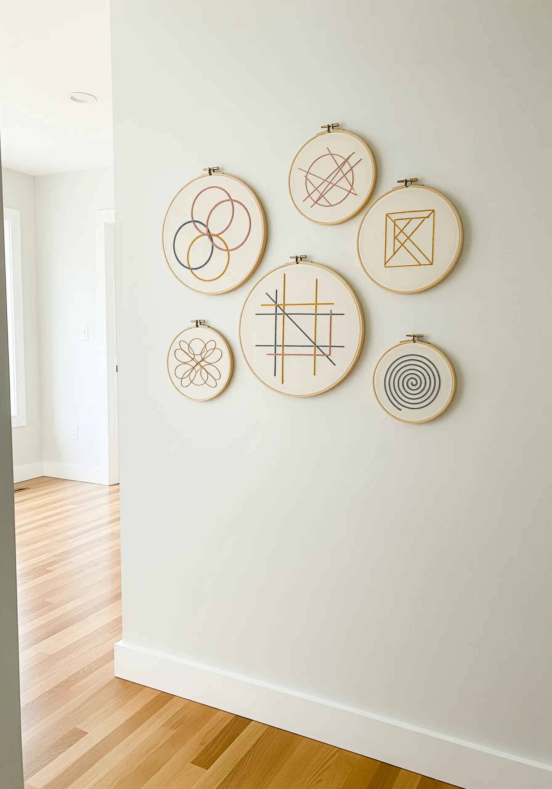A gallery wall of six embroidery hoops with abstract geometric line art in a limited color palette.