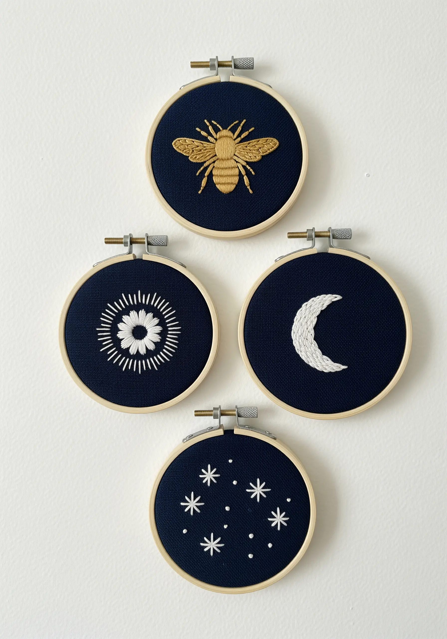 Four small embroidery hoops with celestial motifs in white and gold on navy fabric.