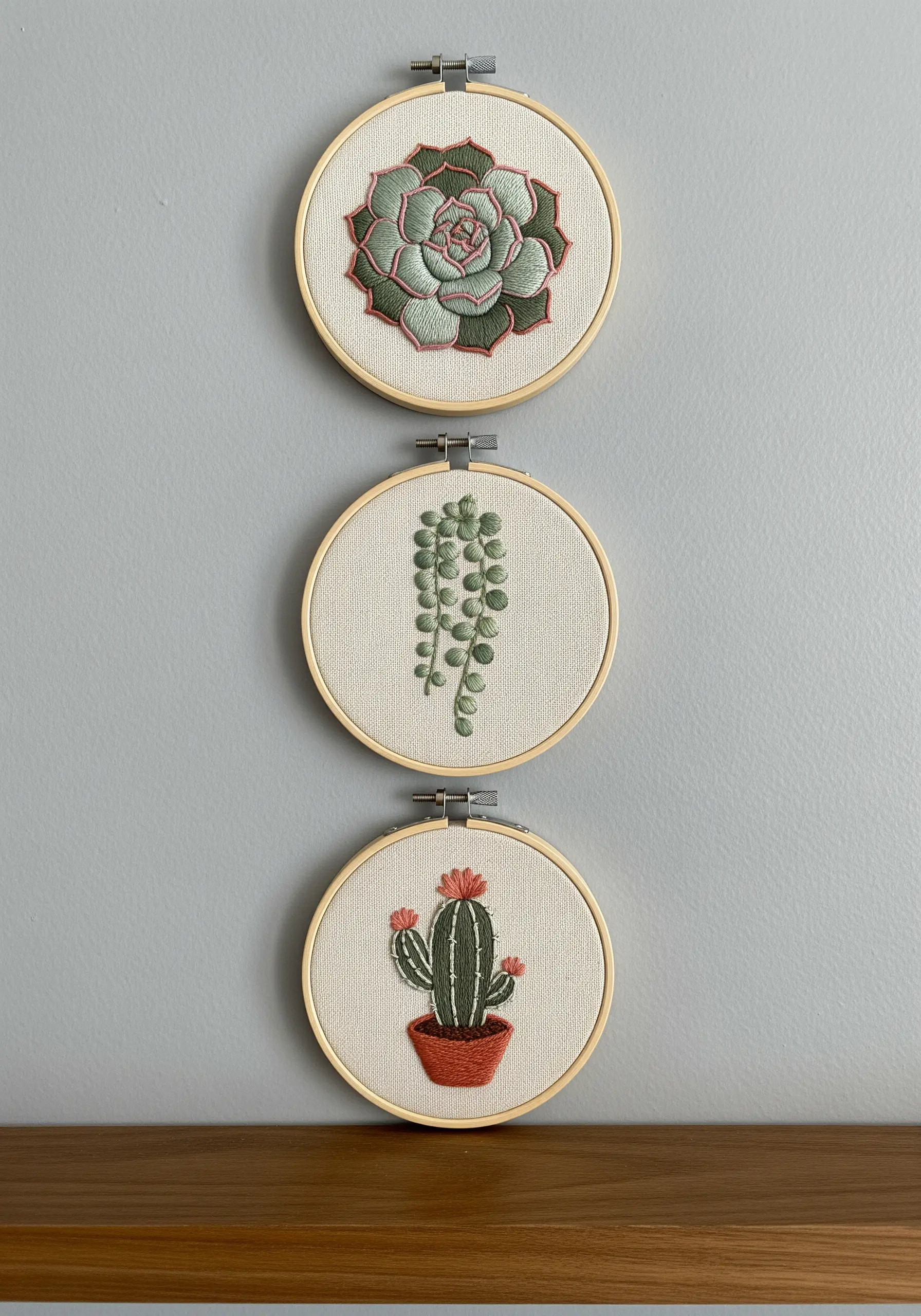A set of three small embroidery hoops, each with a different cross-stitched succulent.