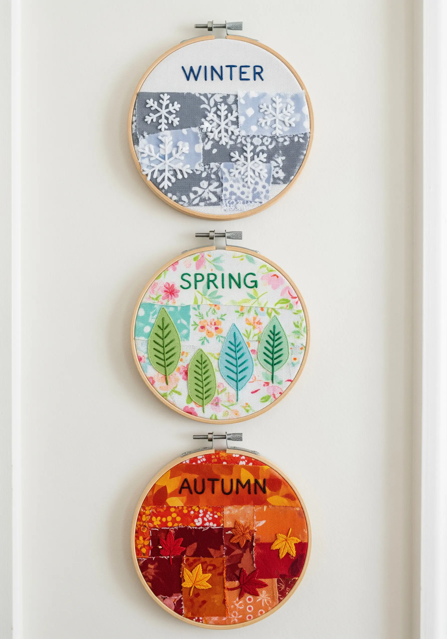 Three embroidery hoops representing winter, spring, and autumn using patchwork and appliqué.