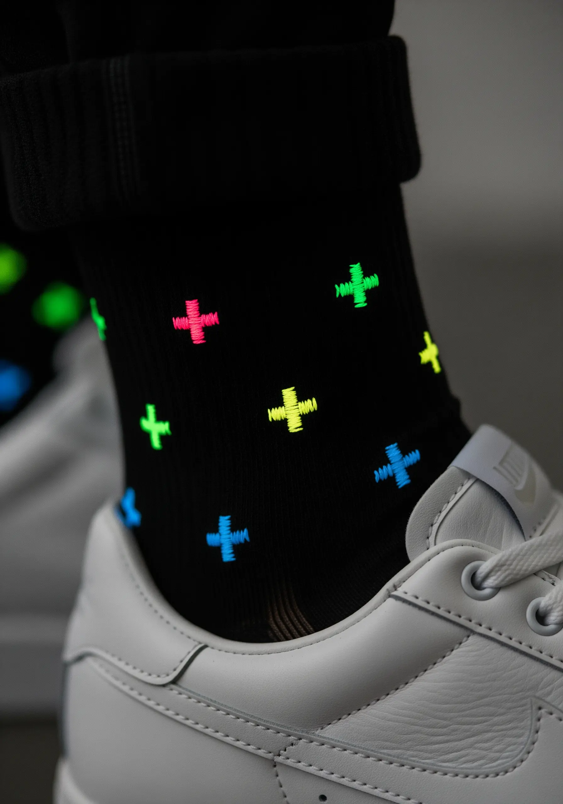 A scattered pattern of small, colorful neon plus signs on a pair of black socks.