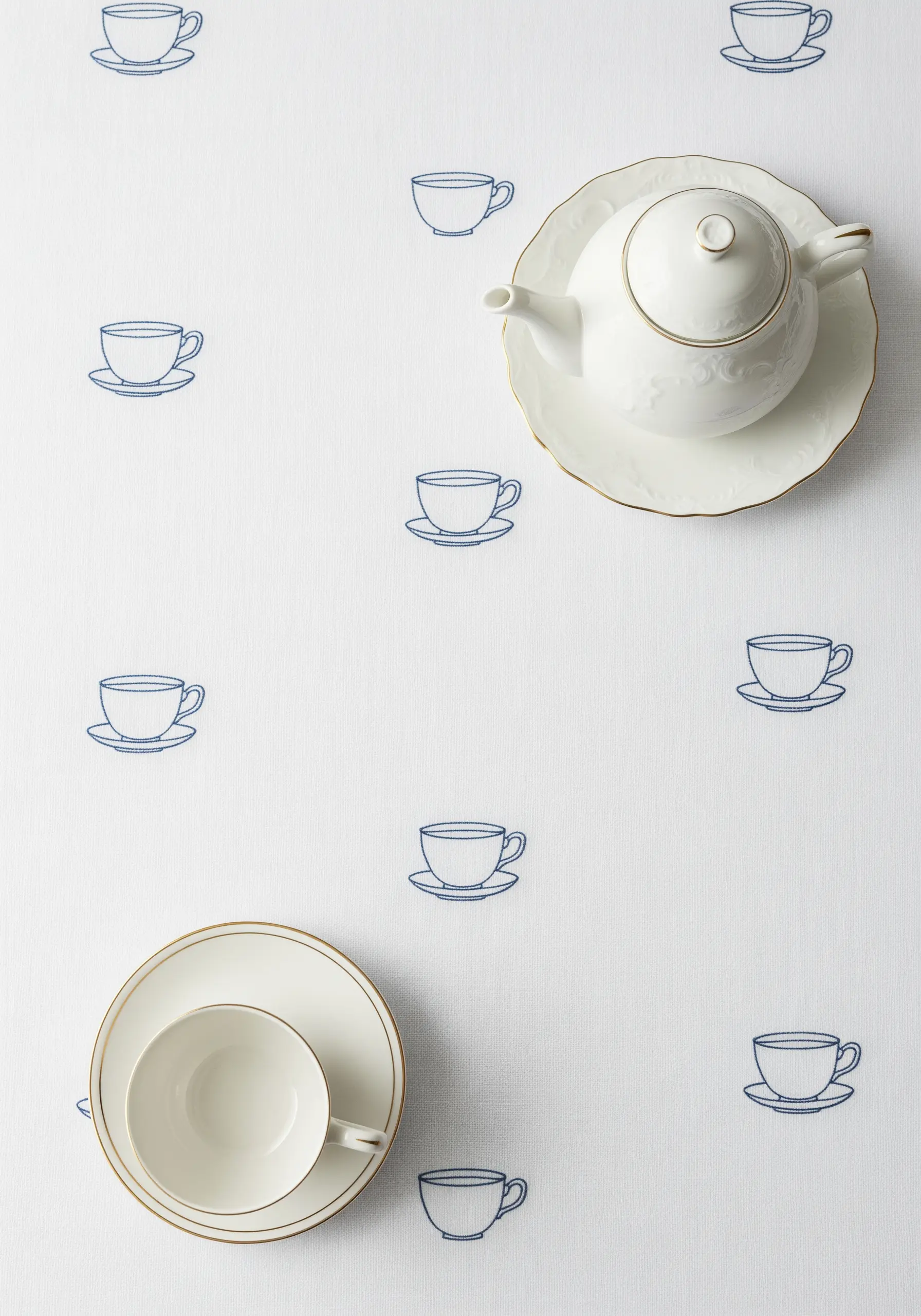 A delicate, scattered pattern of tiny blue teacups embroidered on a white tablecloth.