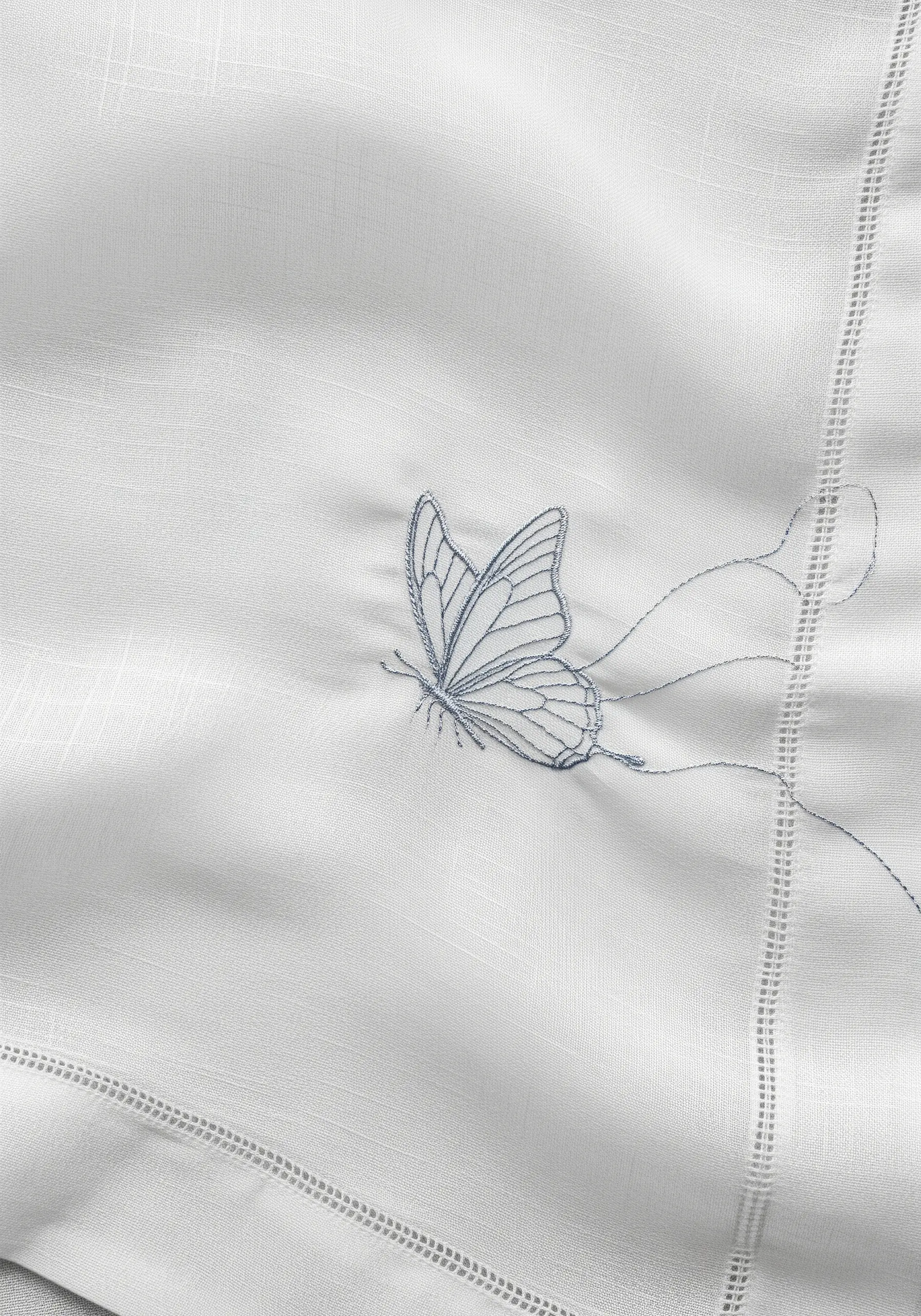 A delicately embroidered butterfly on white linen with long, trailing blue threads.
