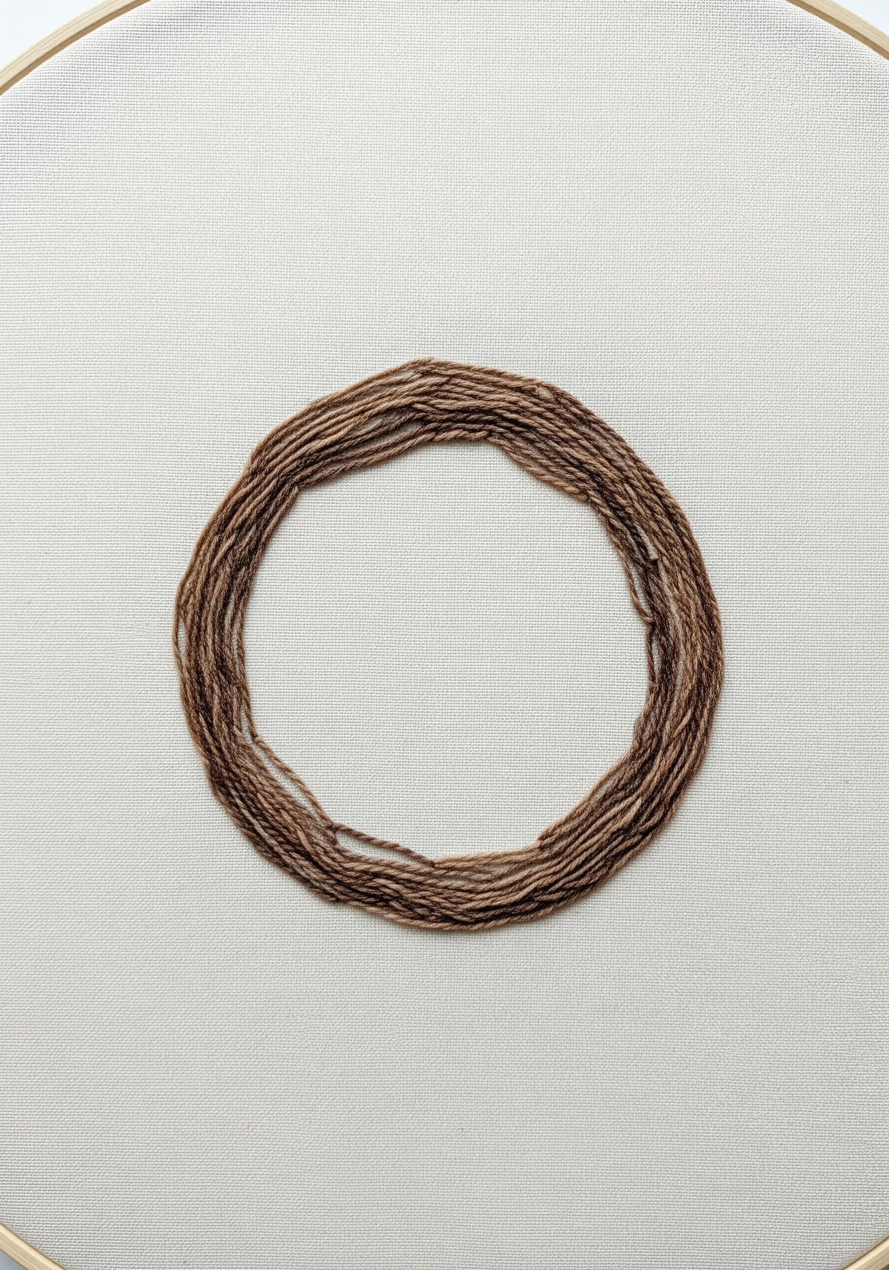A minimalist circle of layered, unwound brown embroidery floss on a neutral linen background.