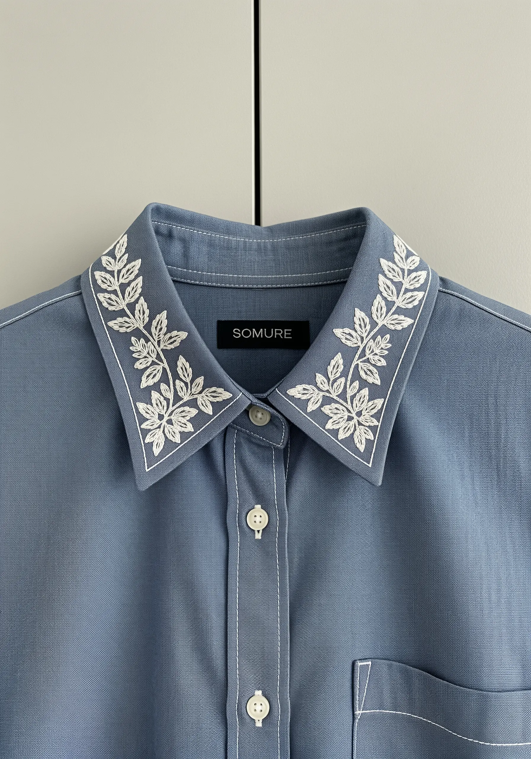 White botanical leaf embroidery decorating the collar of a light blue button-down shirt.