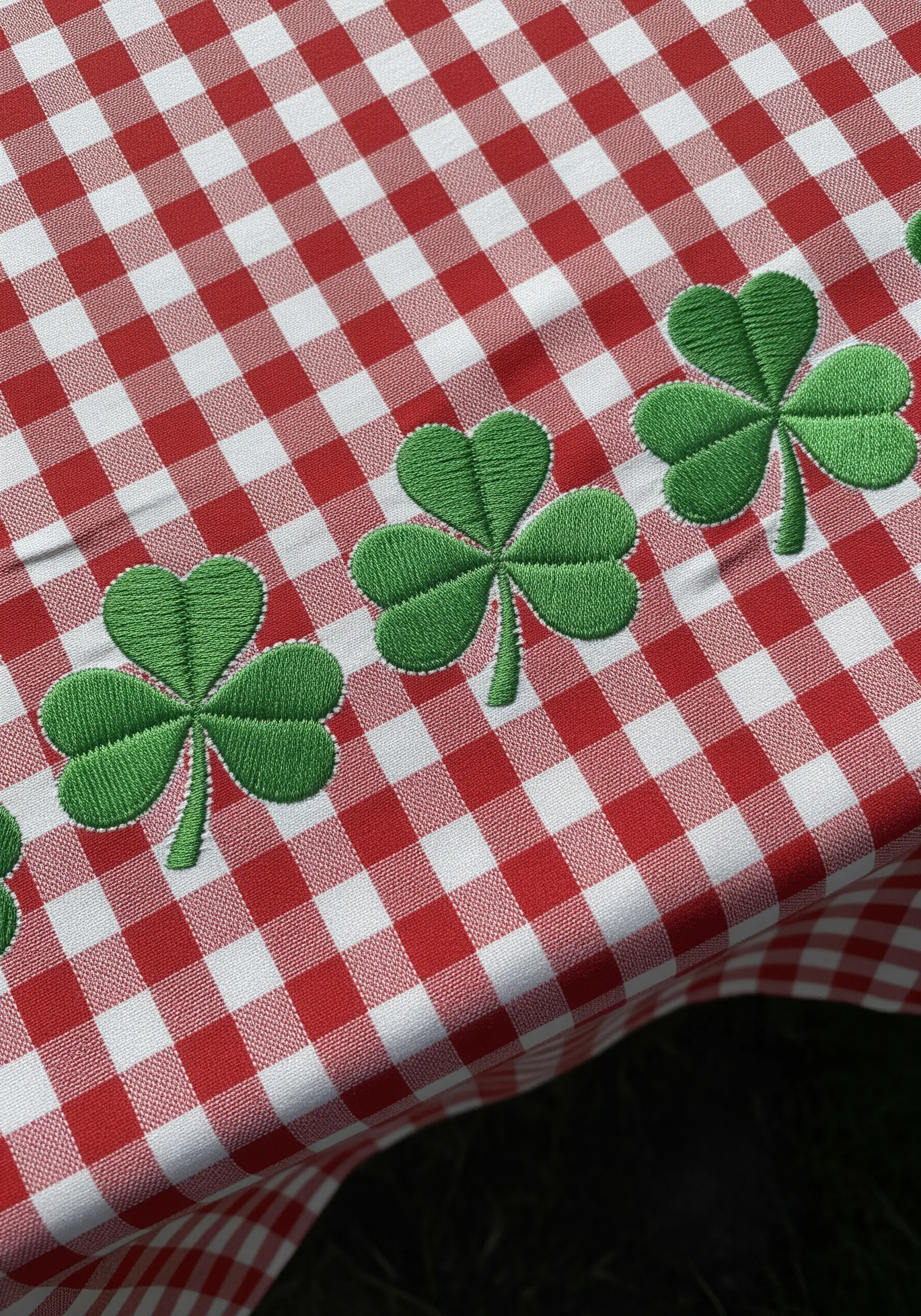 A row of bright green embroidered shamrocks with clean outlines on a red and white gingham tablecloth.