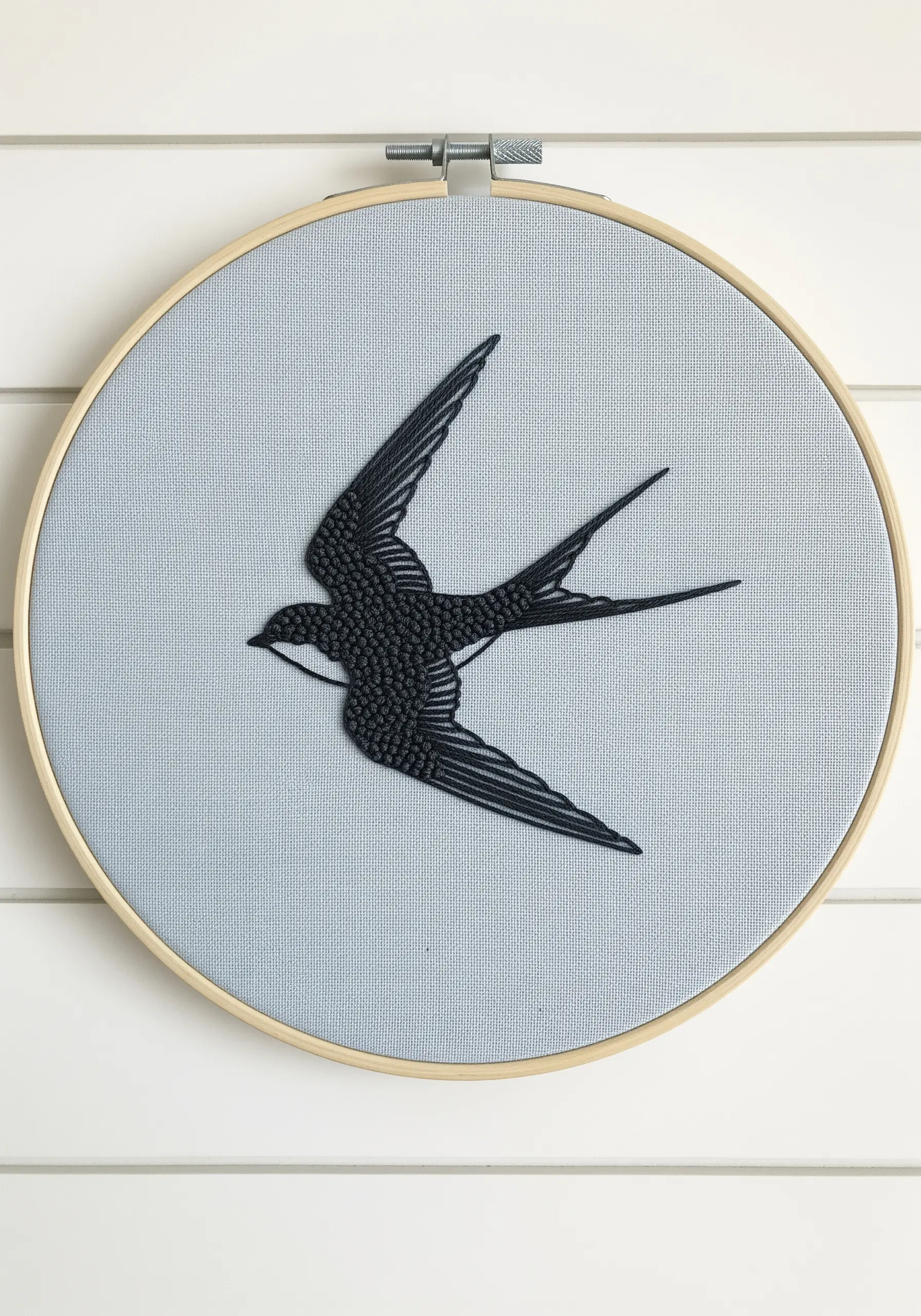 An embroidered swallow silhouette filled with dense black French knots on blue fabric.