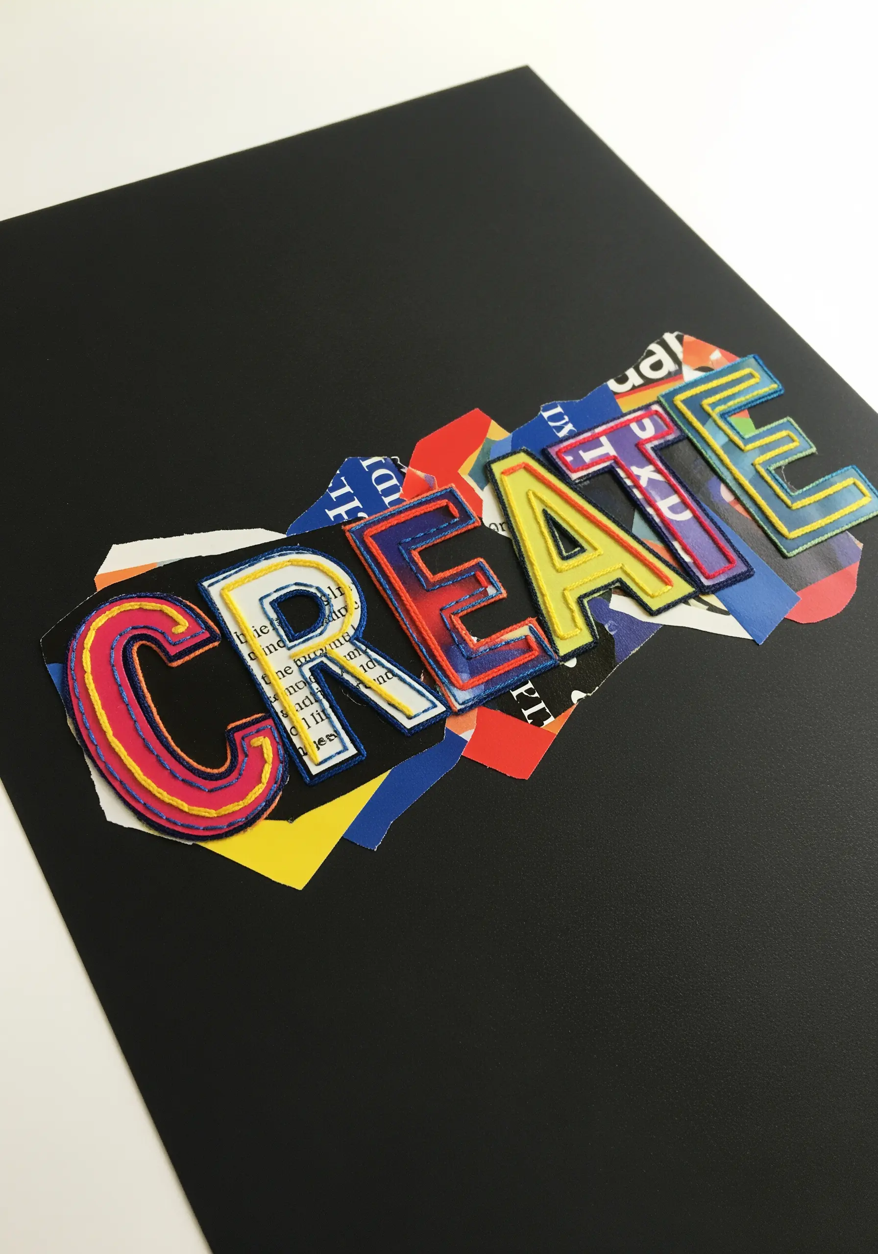 The word CREATE in colorful appliqué letters outlined in embroidery on a paper collage.