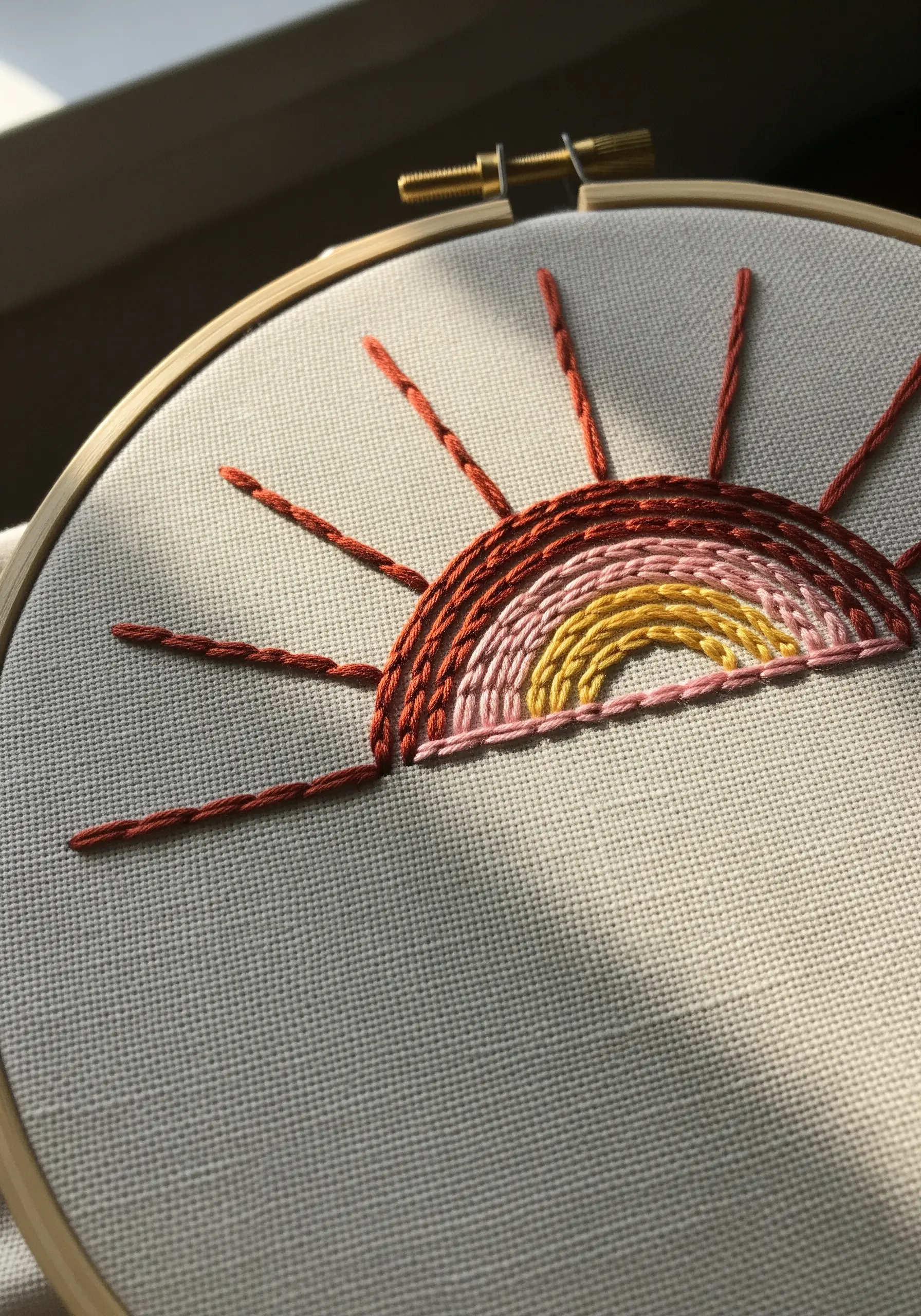 Embroidered sunset with clean, concentric arcs in red, pink, and yellow.