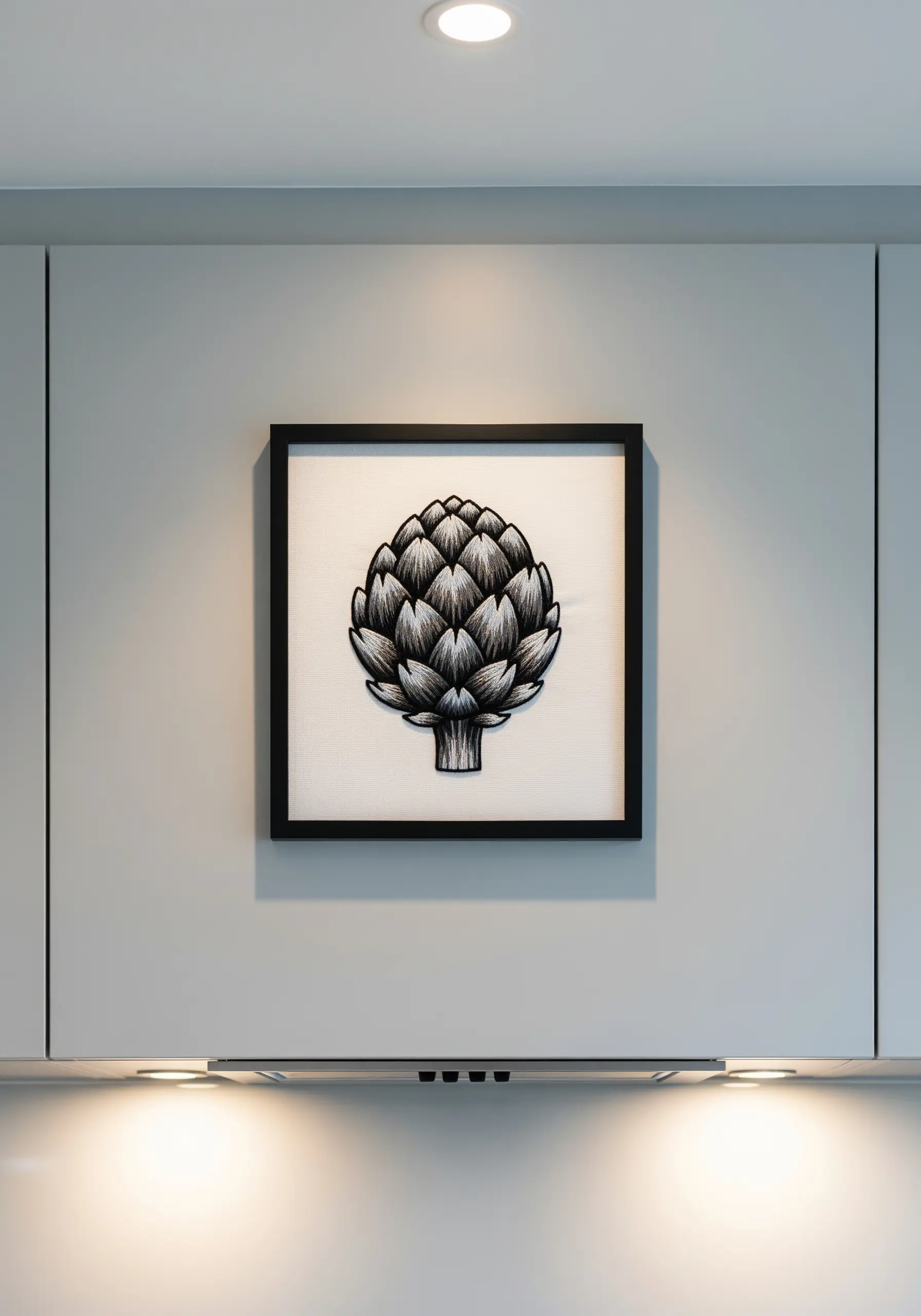 Framed embroidery of a black and white artichoke hanging on a gray kitchen wall.
