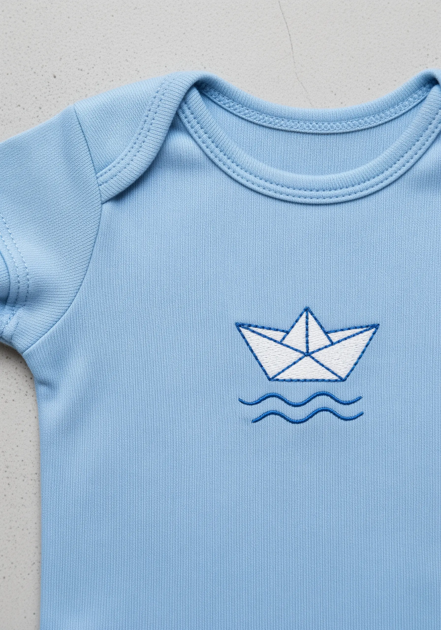 A white and blue embroidered paper boat with clean outlines on a blue bodysuit.