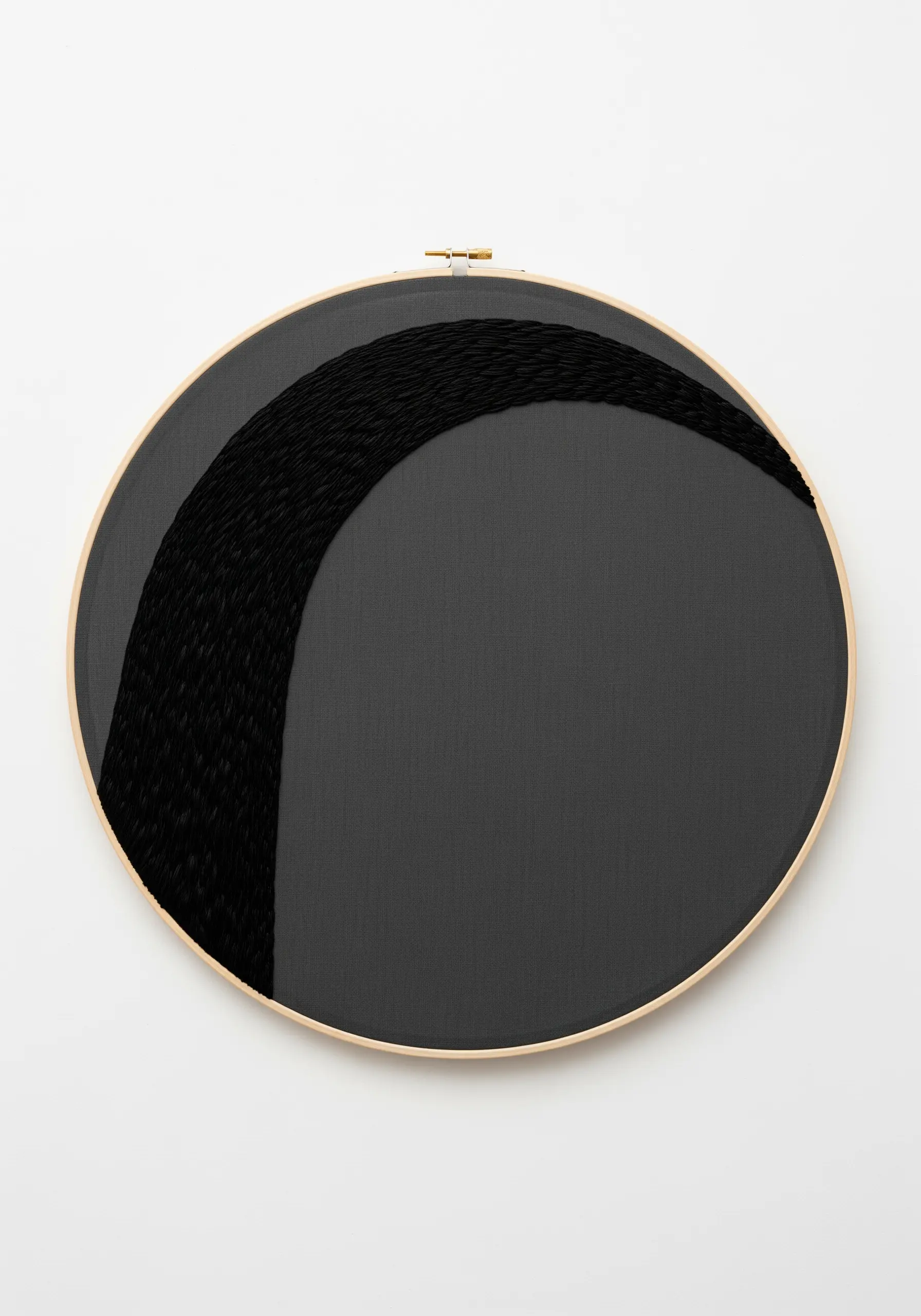 Dense black satin stitch in an arch shape on black fabric in a wooden hoop.