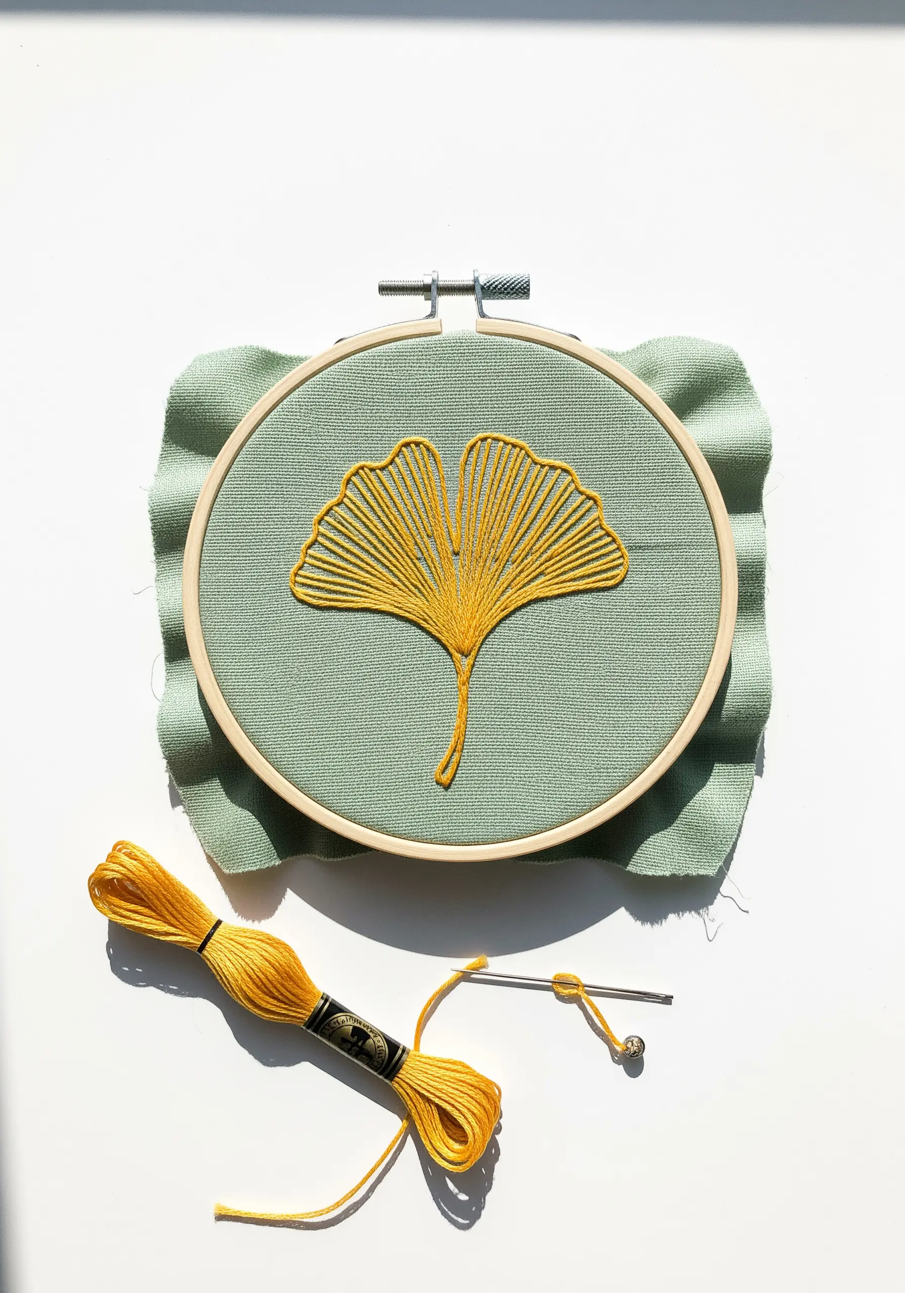 A stylized ginkgo leaf created with radiating straight stitches in yellow.