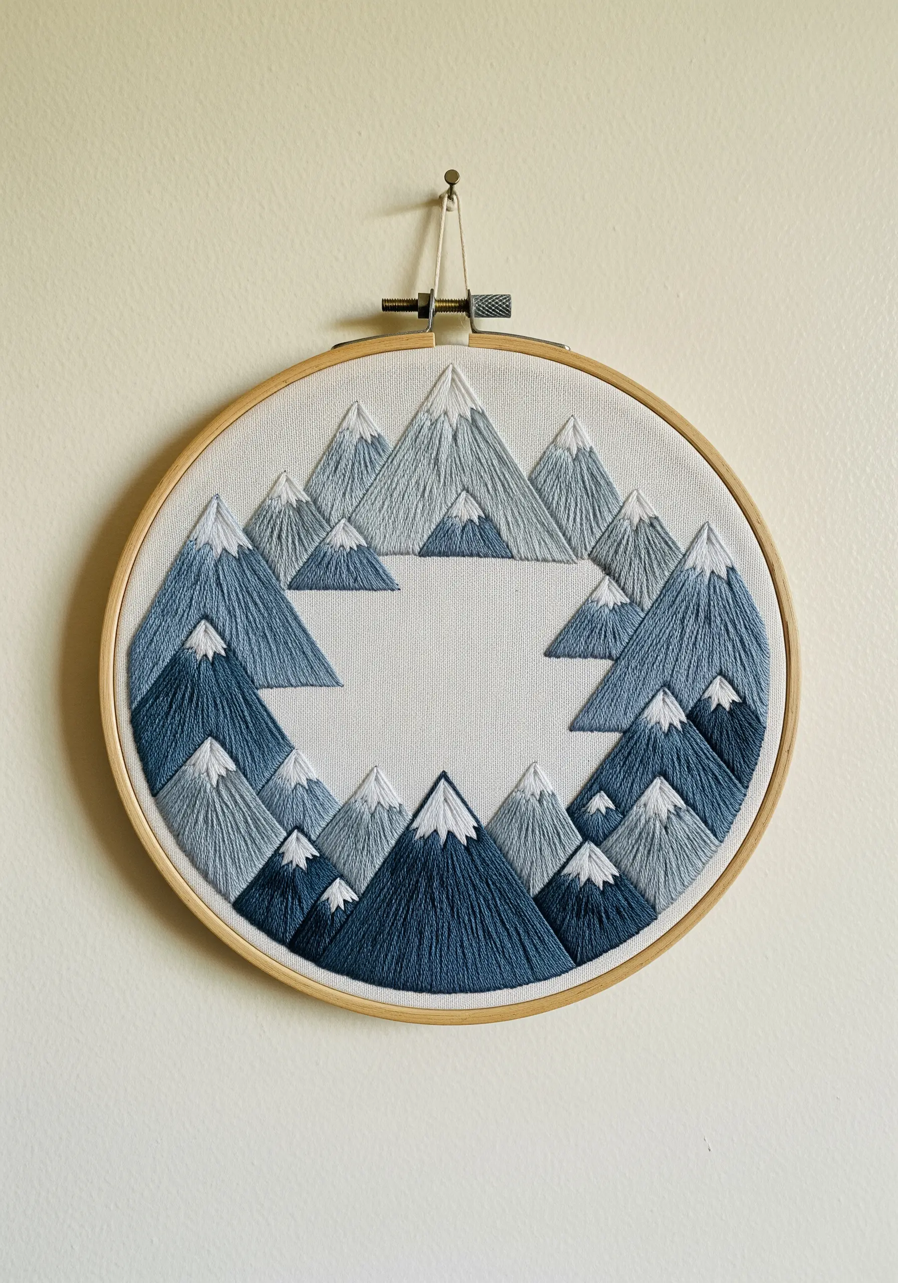 A mandala of stylized mountains in shades of blue with satin stitch.