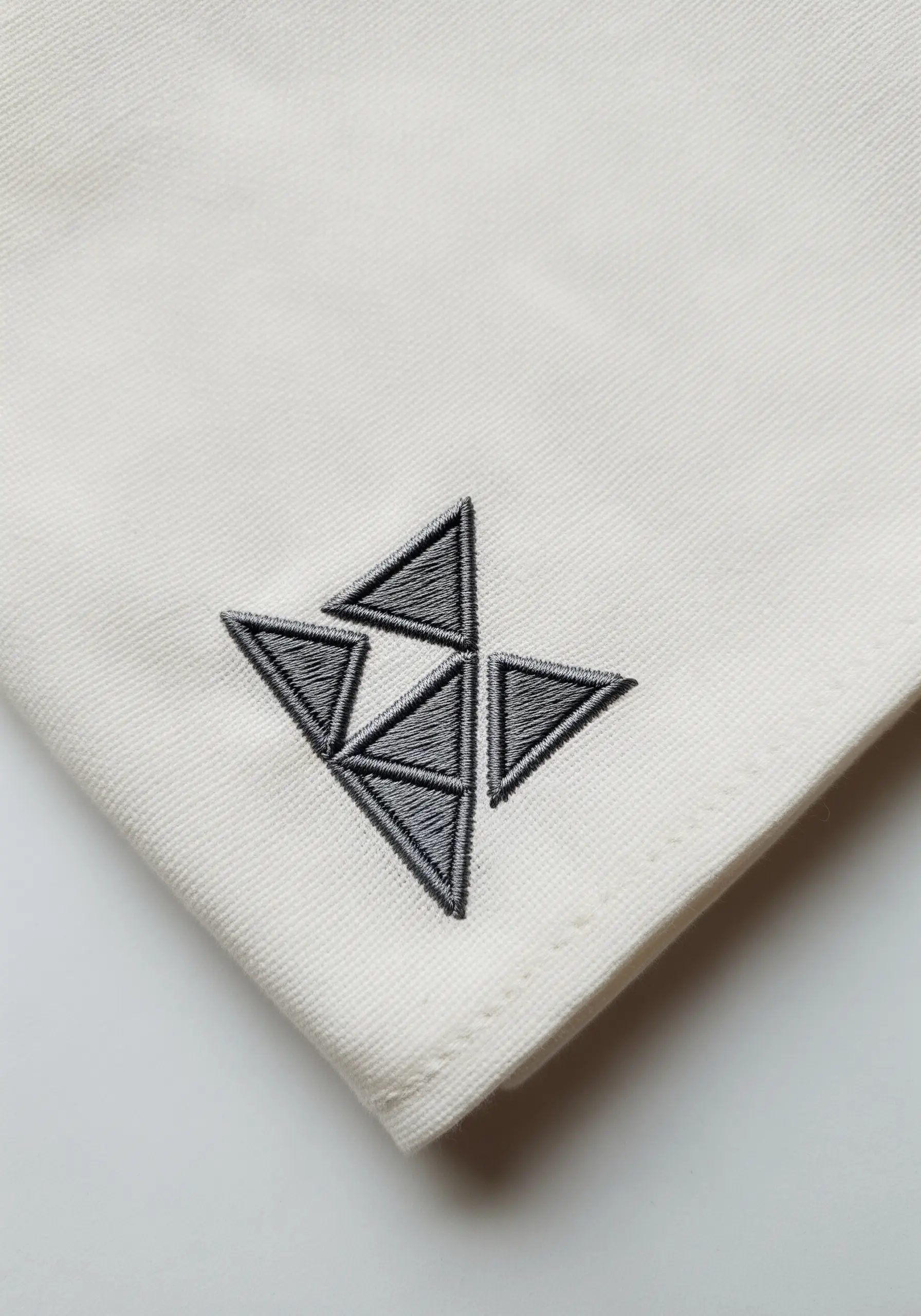 A modern geometric motif of interlocking triangles stitched in grey thread on a cream handkerchief.