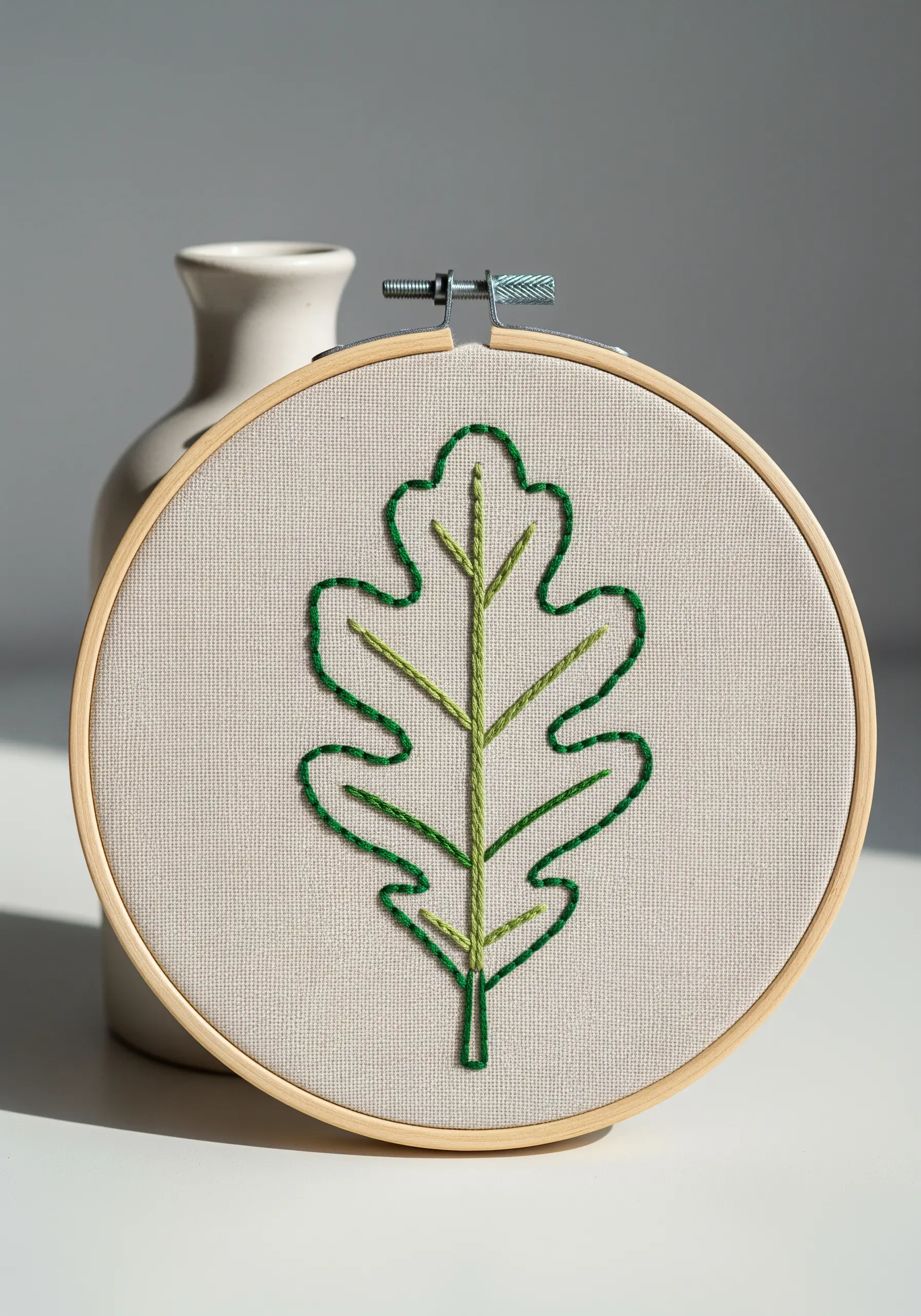A green outline of an oak leaf with lighter green veins embroidered in a hoop.