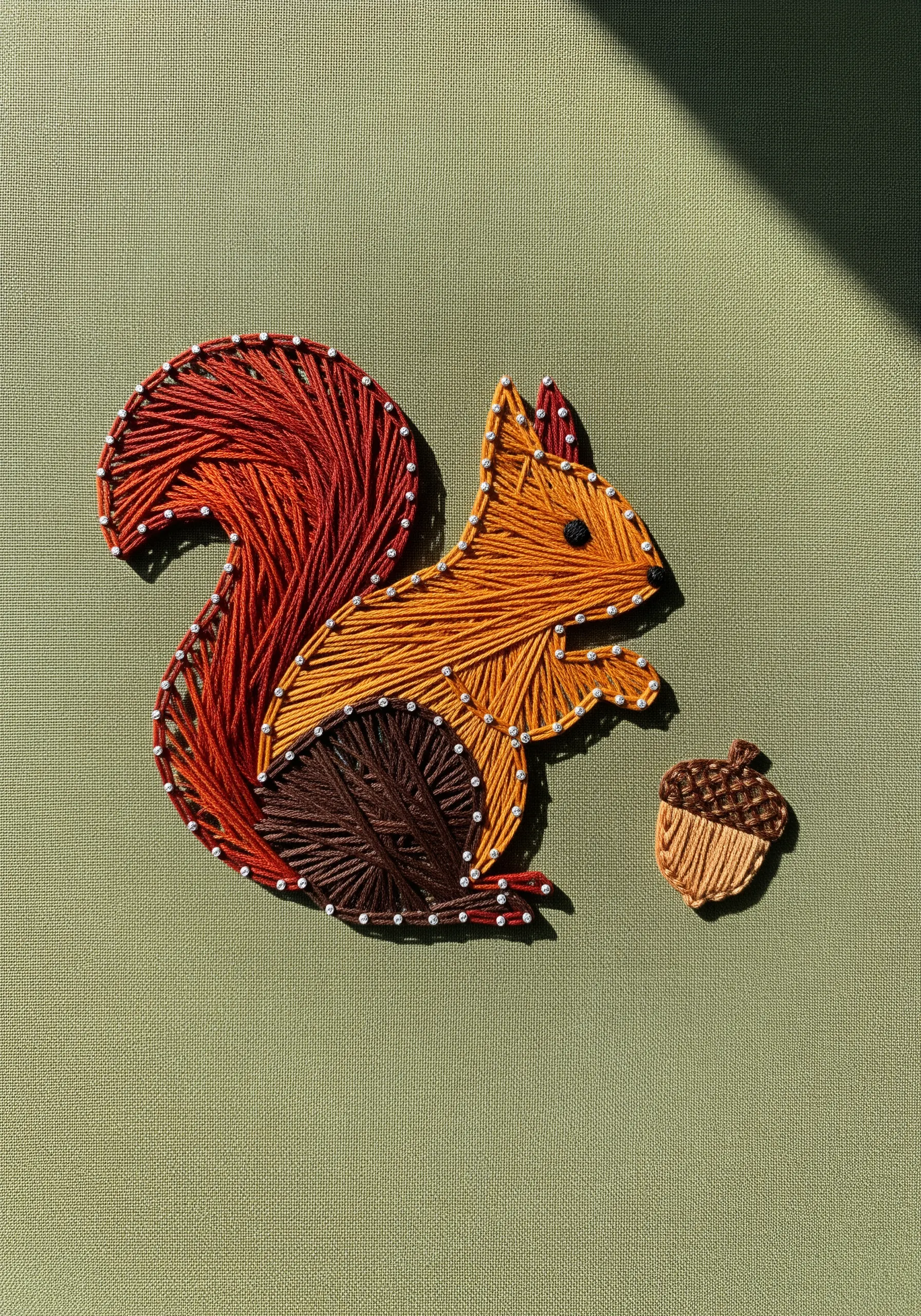 Color-blocked embroidery of a squirrel in orange, red, and brown, with a small acorn.