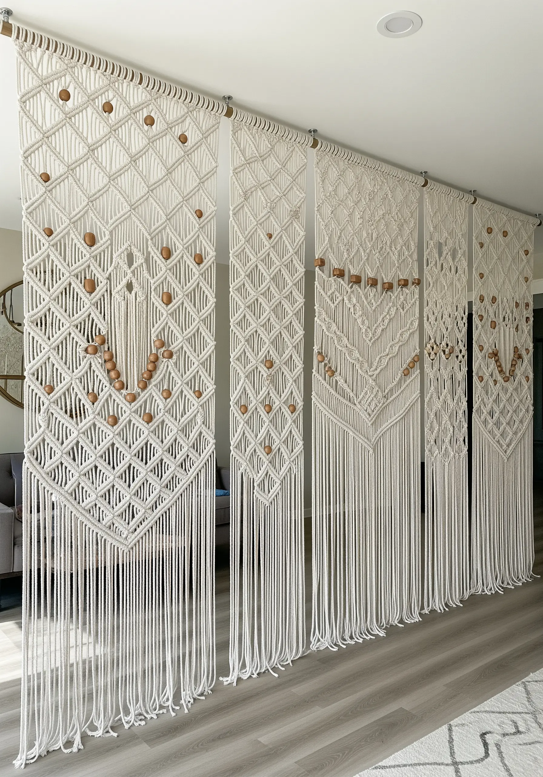 Four large macrame panels with wooden beads acting as a room divider in an open-plan space.