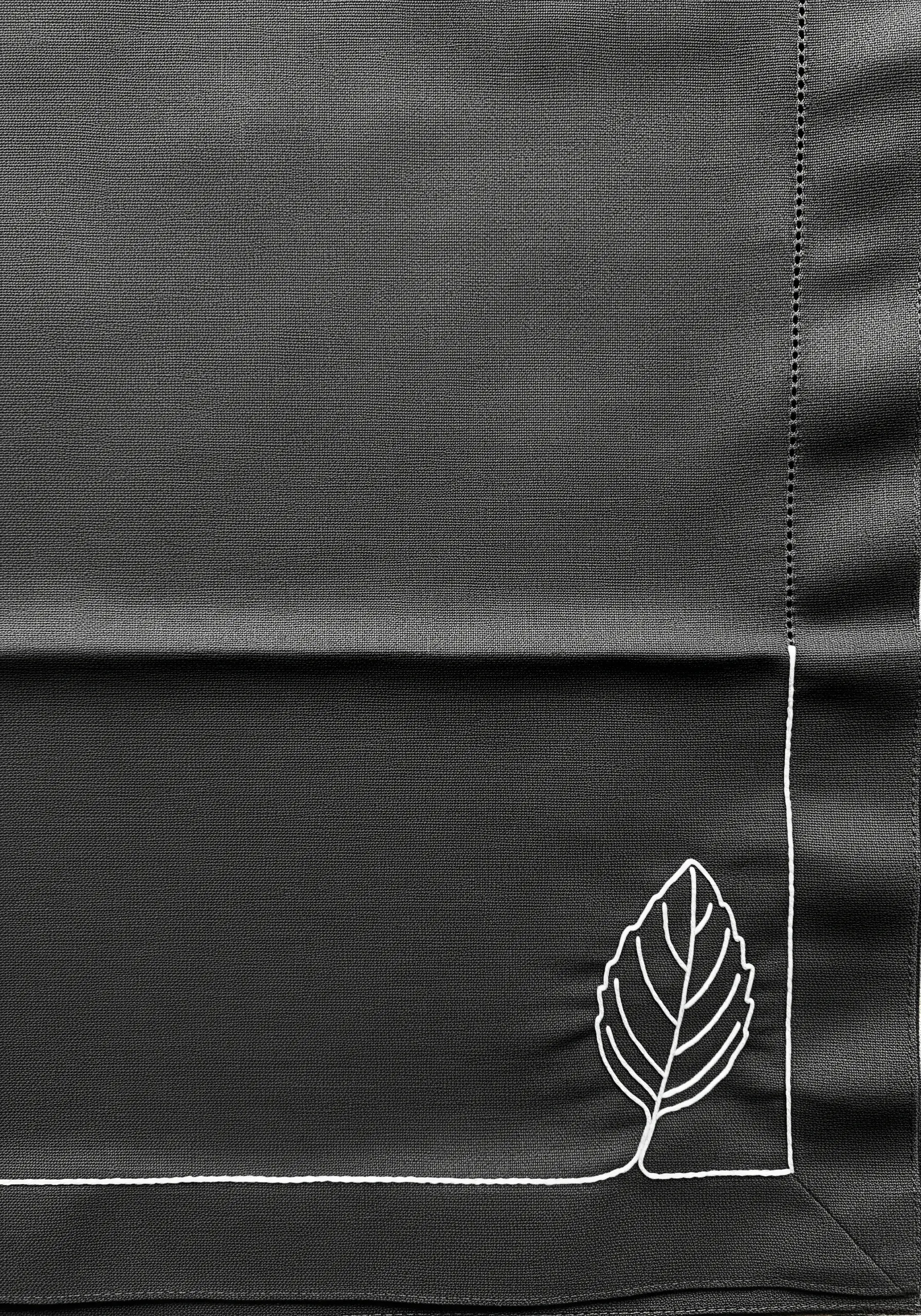 A single white line embroidered on a dark napkin, forming a border and a leaf in the corner.