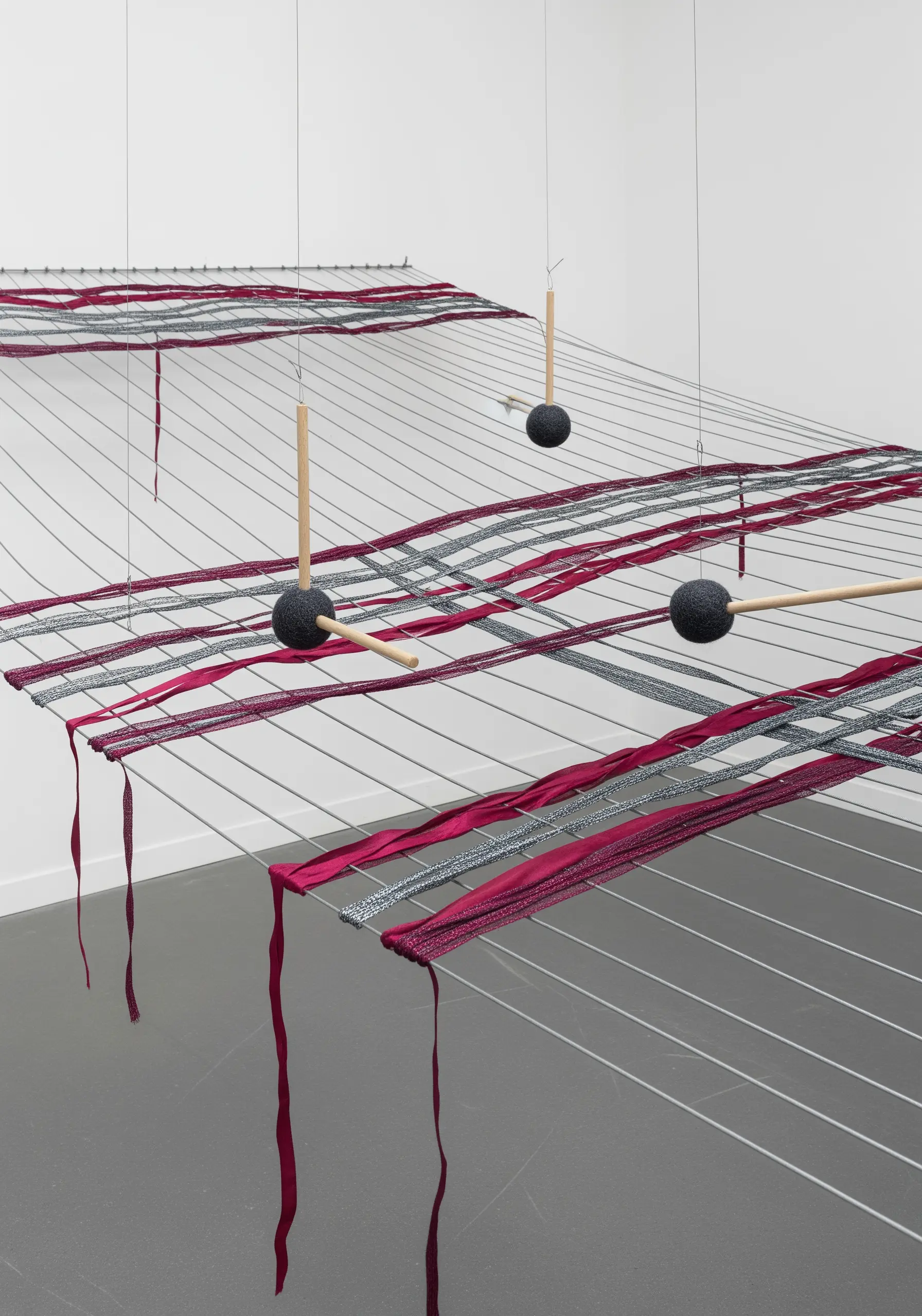 A suspended installation of tightly stretched horizontal threads with bands of pink and silver fabric.