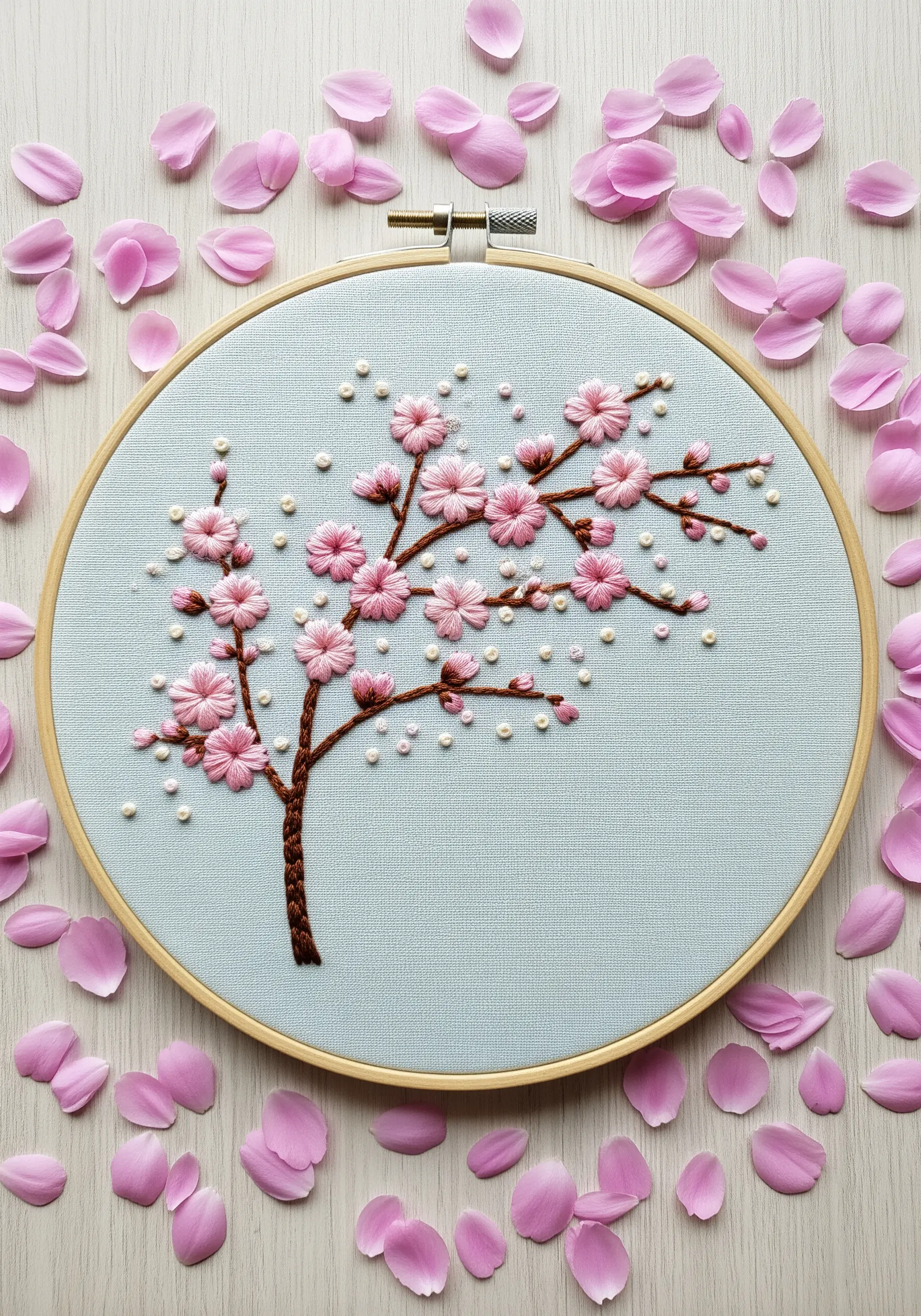 Embroidered cherry blossom tree with pink flowers and scattered pearl beads on blue fabric.