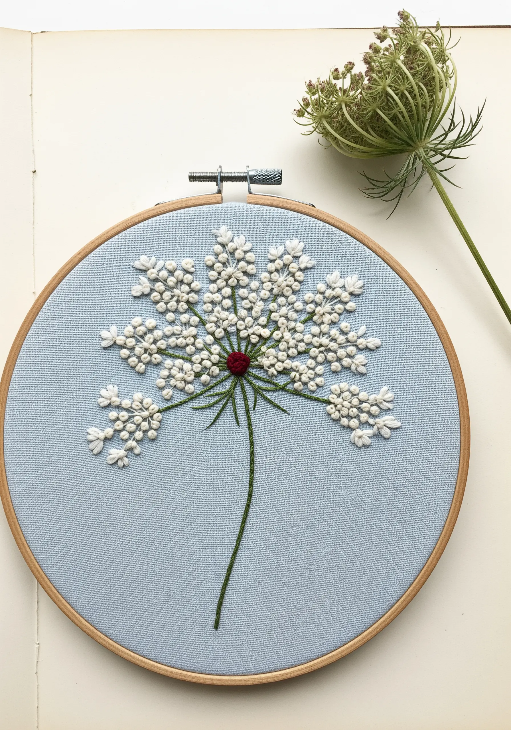 Embroidered Queen Anne's Lace with white colonial knots and a red center on blue fabric.