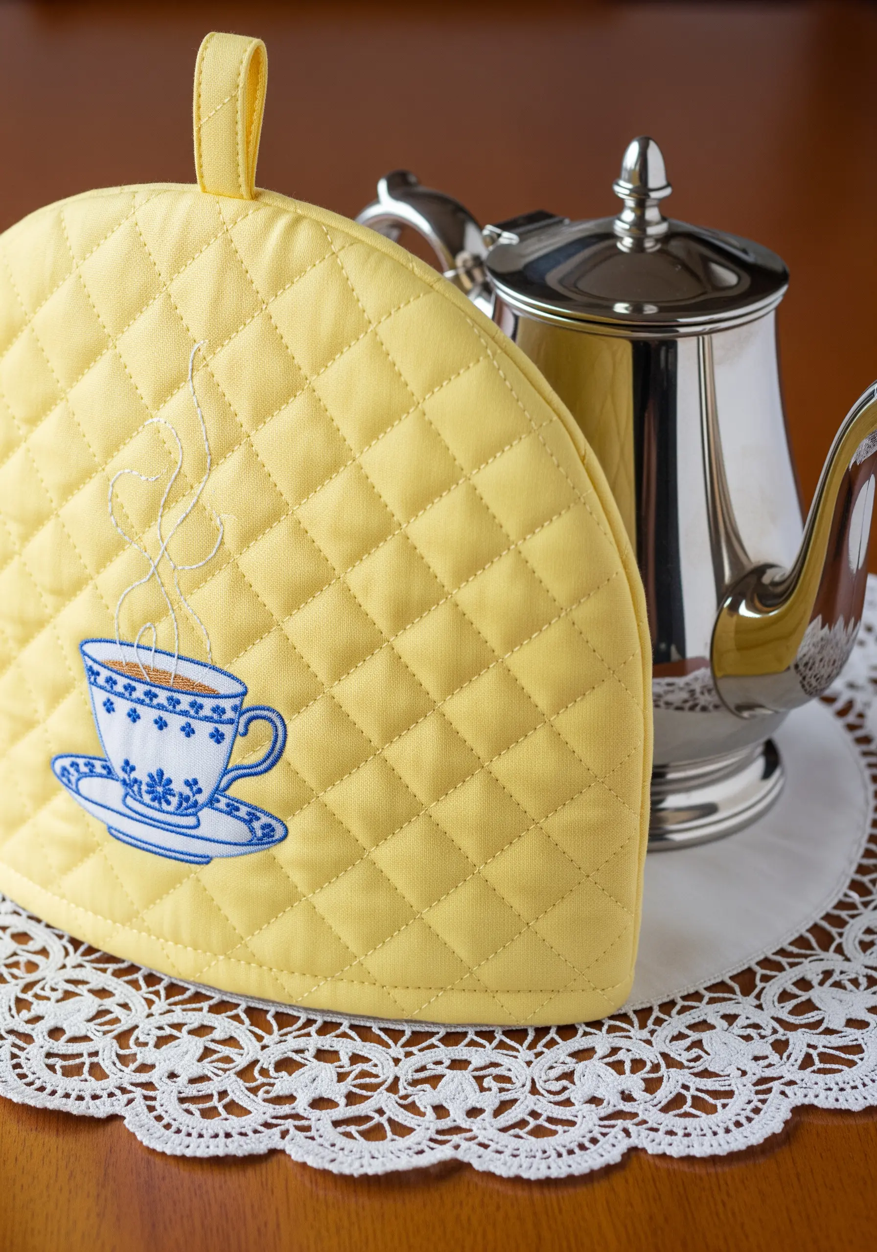 A single-thread embroidery of a teacup with rising steam on a yellow quilted tea cozy.