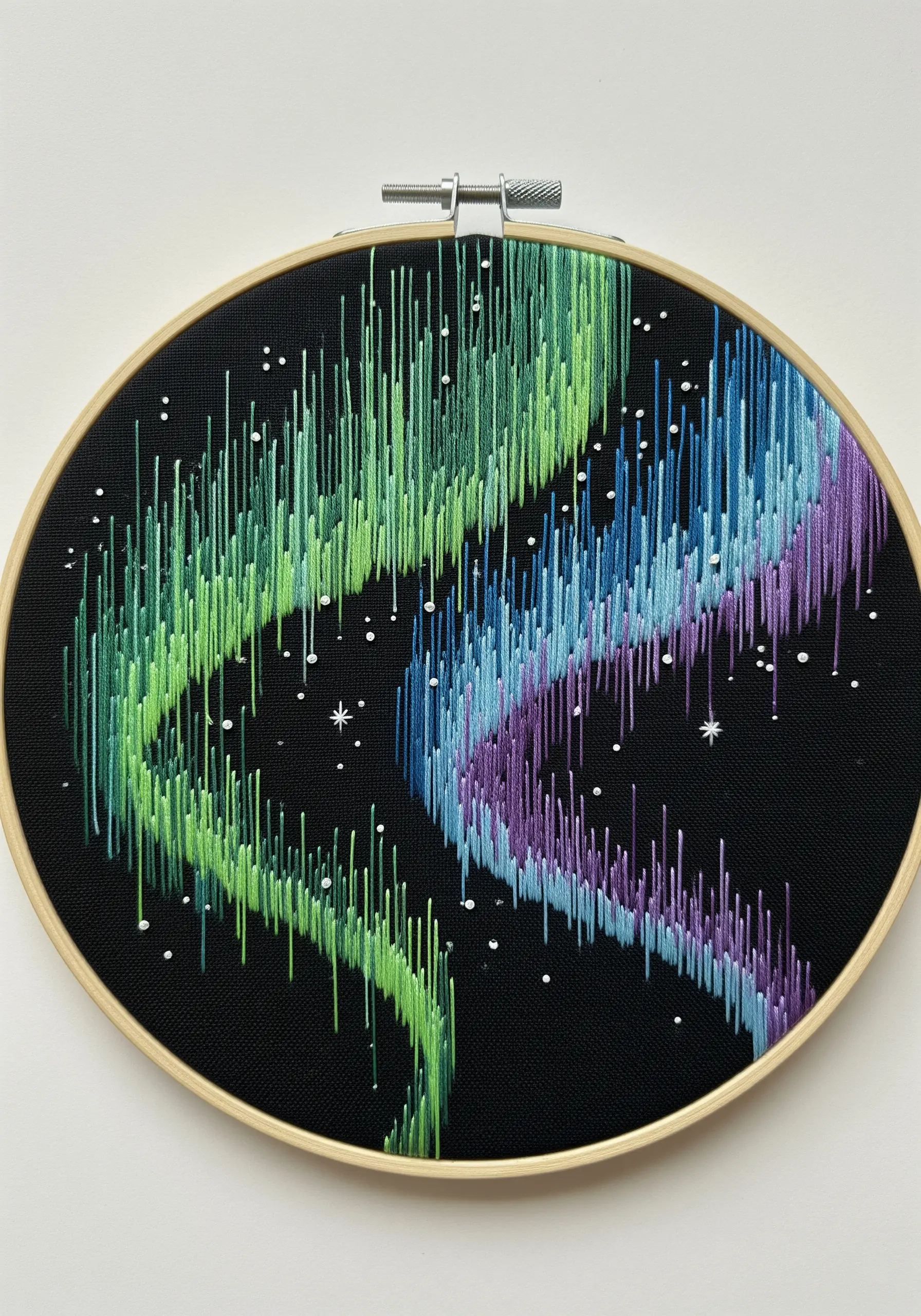 Embroidery of the aurora borealis with long green, blue, and purple vertical stitches on black fabric.