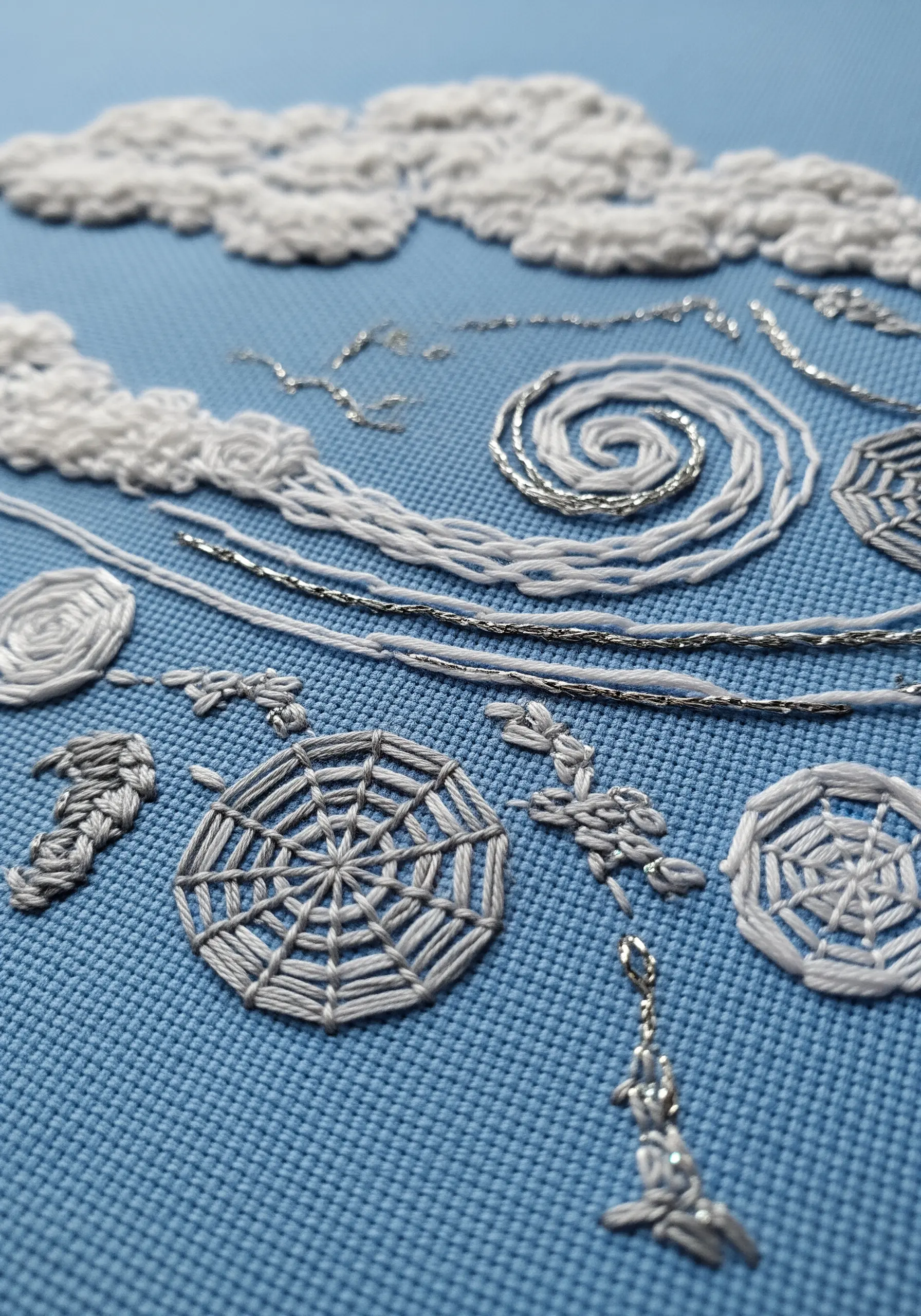 Close-up of white and silver embroidered frost patterns on blue fabric.