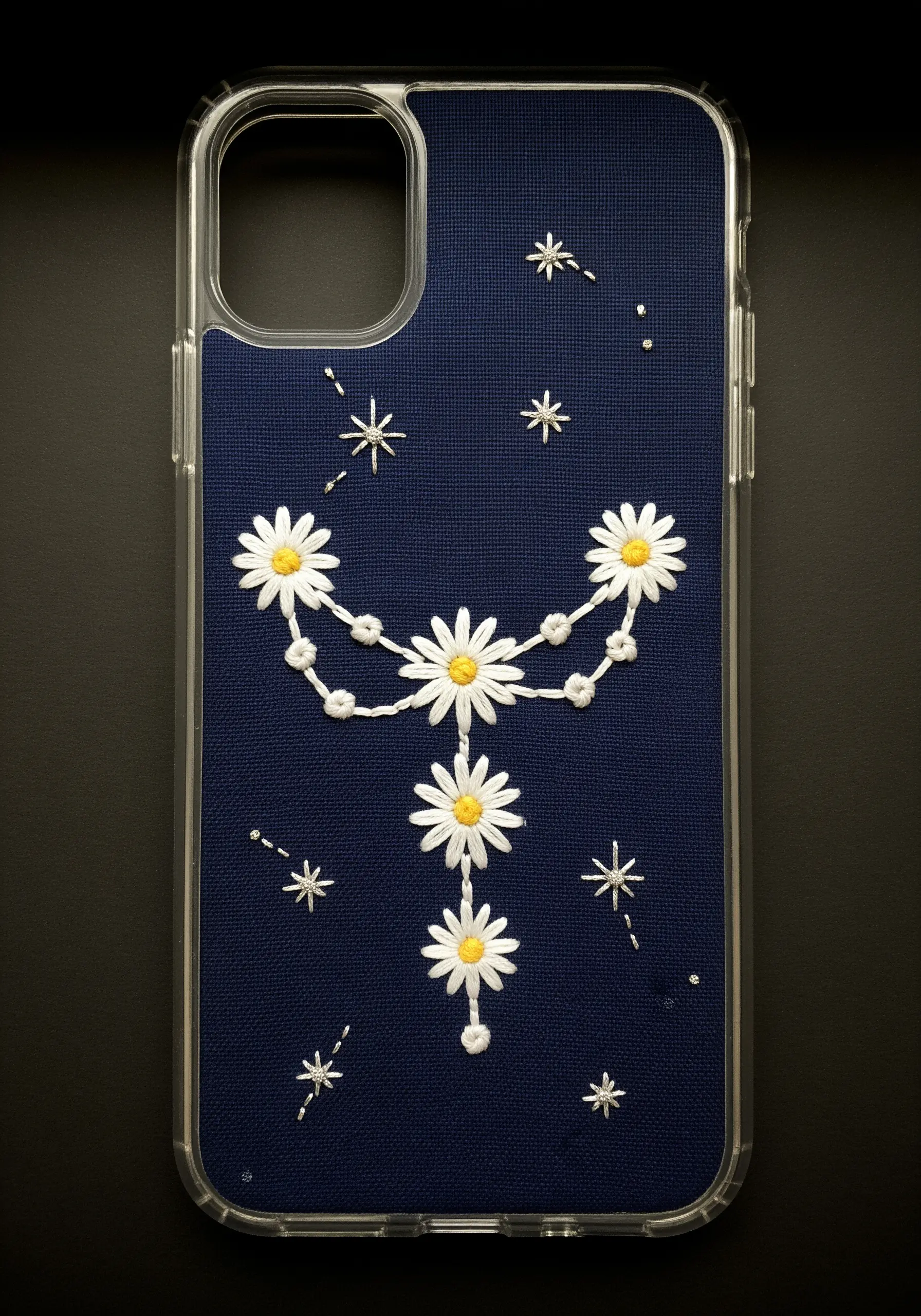 Embroidered daisies arranged like a celestial constellation on a dark blue phone case.