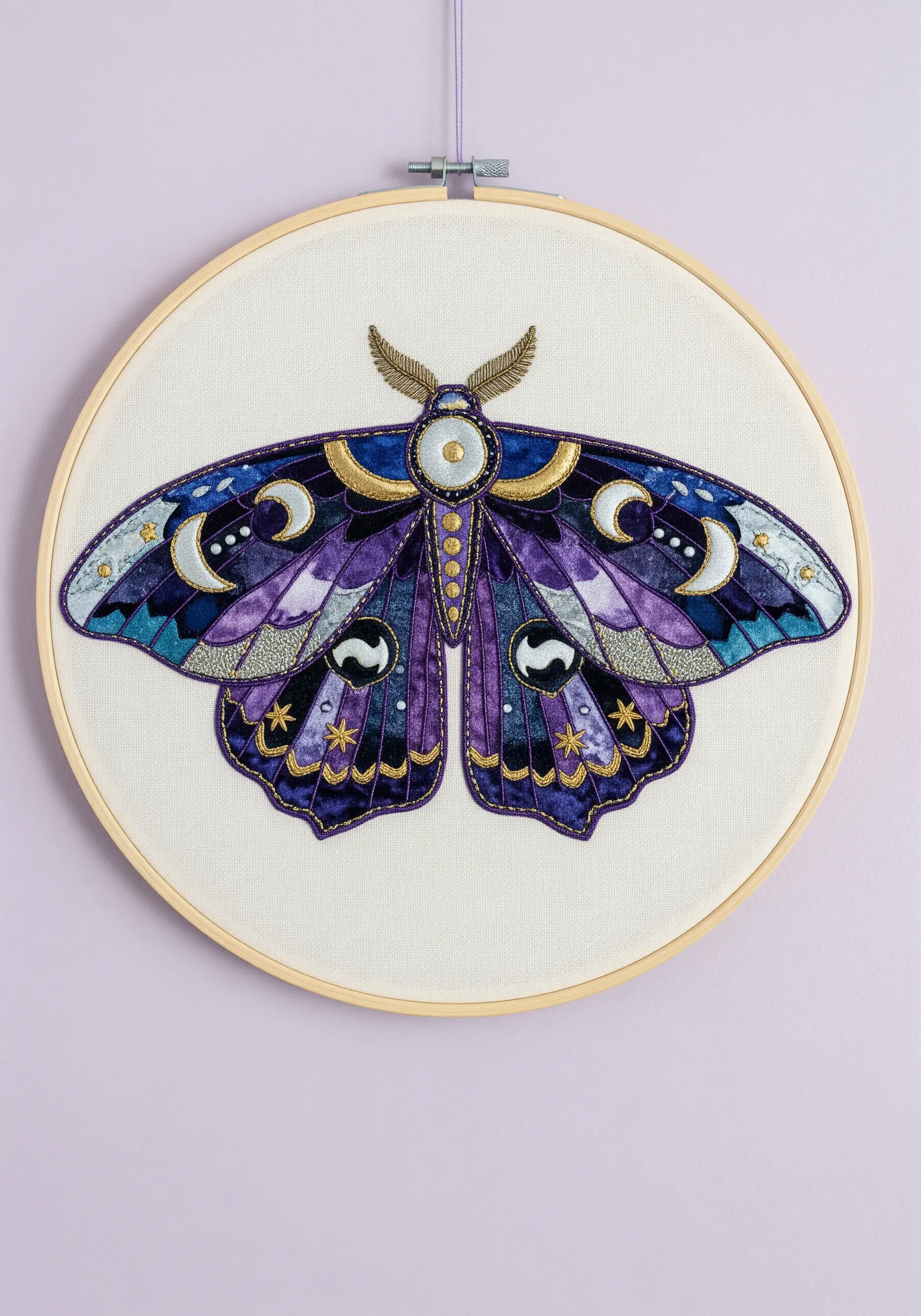 A celestial moth with wings made from purple and blue satin fabric, outlined in gold thread.
